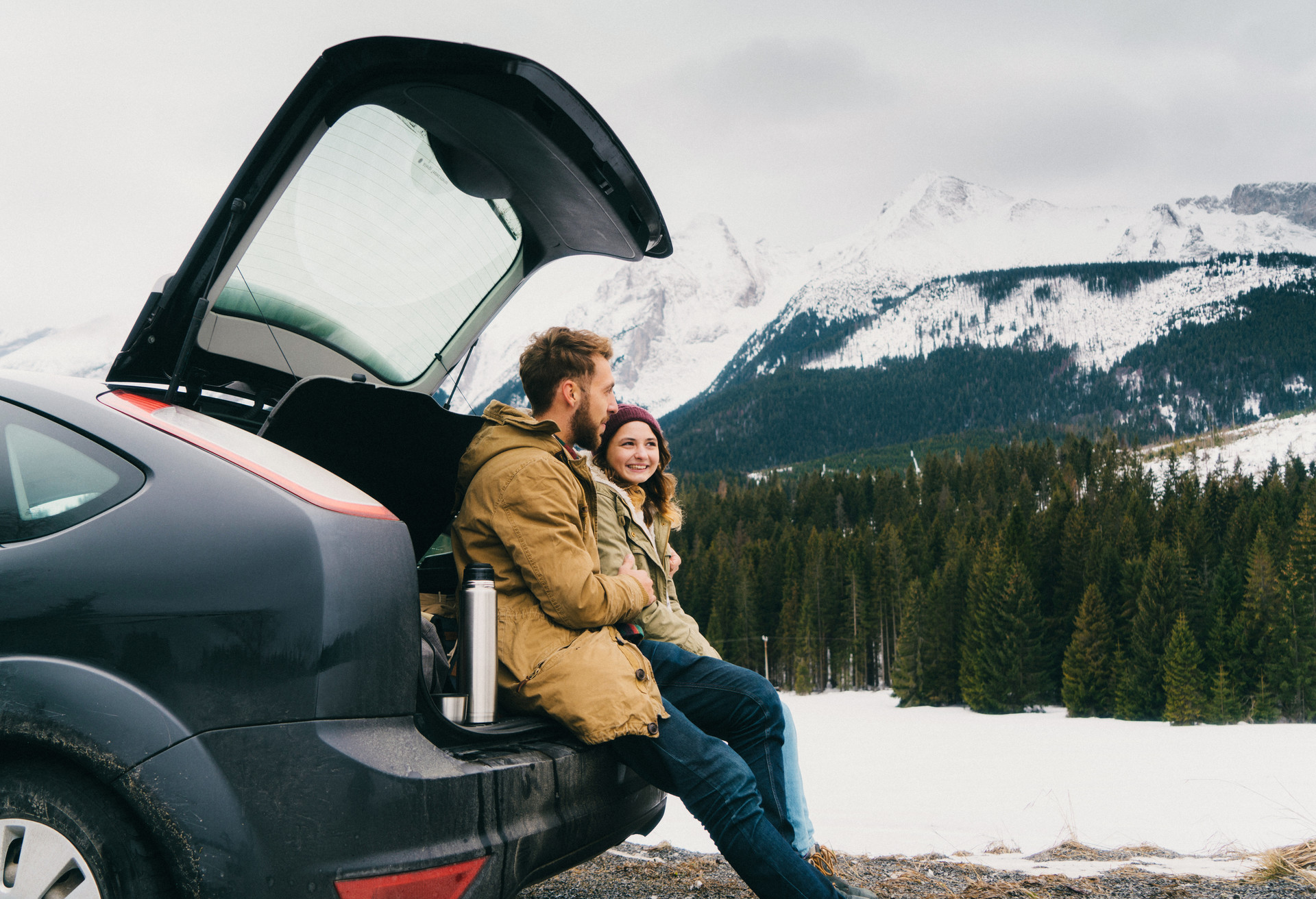 Young Caucasian couple resting near the car in mountains in winter