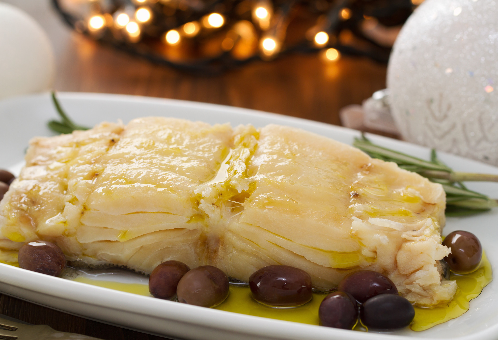 boiled cod fish with oil and olives on white dish