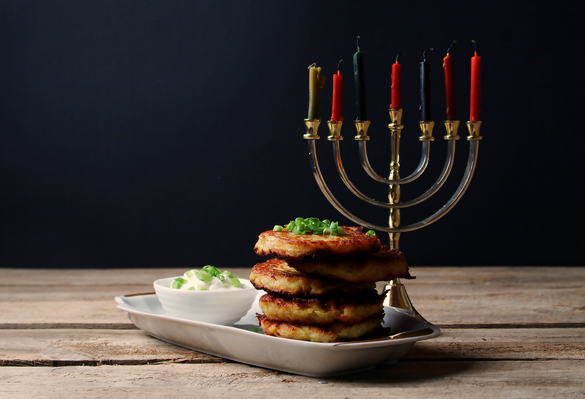Traditional Hanukkah Jewish Cuisine. Latkes With Sour Cream And Menorah On Wooden Table And Black Background. Side View, Copy Space.; Shutterstock ID 1544546174; Purpose: Virtual Christmas Guides; Brand (KAYAK, Momondo, Any): Kayak; Client/Licensee: KAYAK