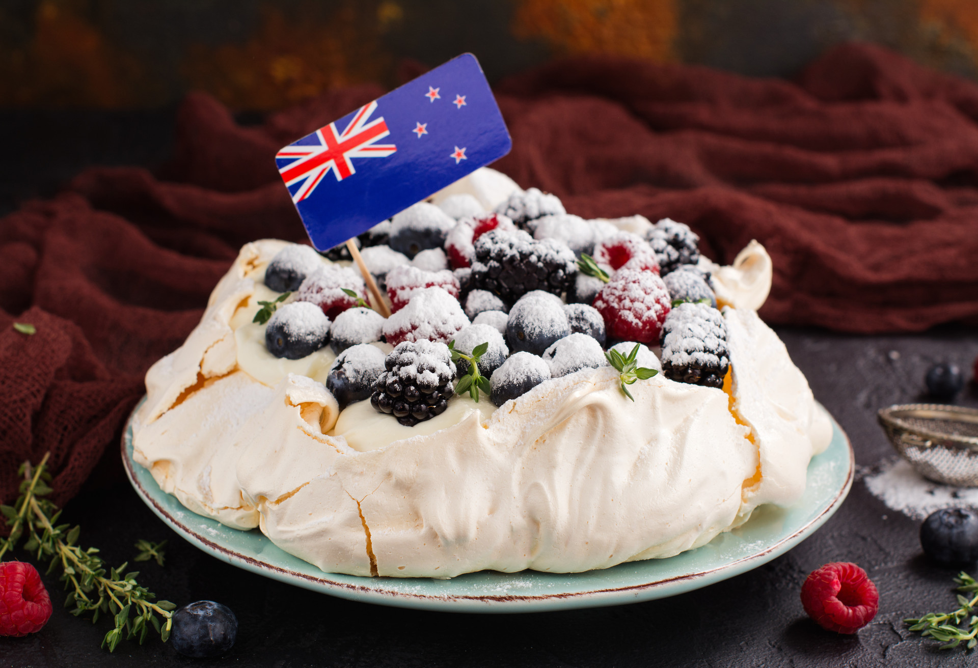 Delicious Pavlova cake with cream, berries thyme and New Zealand flag over dark background. Space for text. Selective focus; Shutterstock ID 530911201; Purpose: Virtual Christmas Guides; Brand (KAYAK, Momondo, Any): Kayak; Client/Licensee: KAYAK