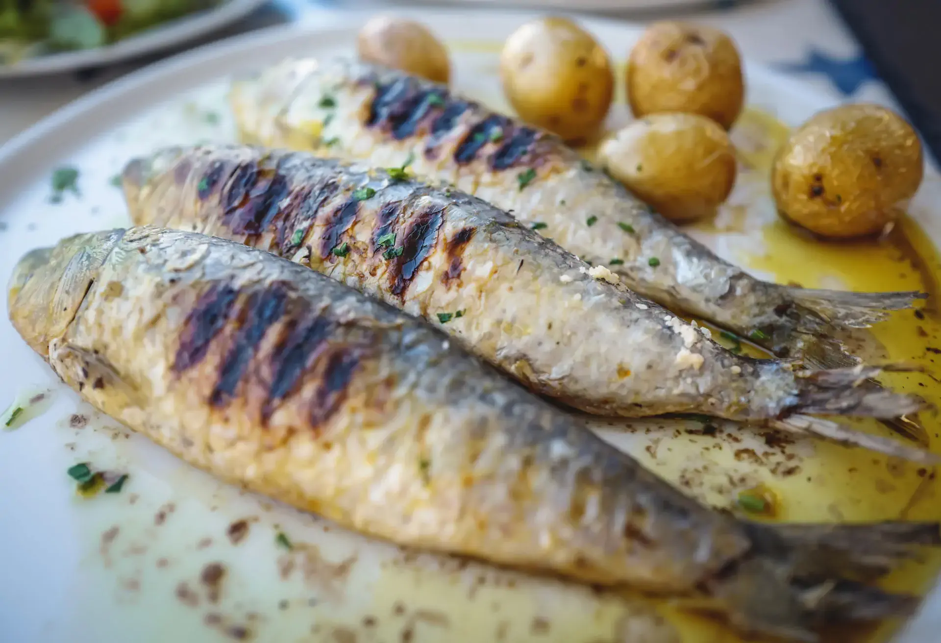 3 grilled whole sardines on a plate with small potatoes