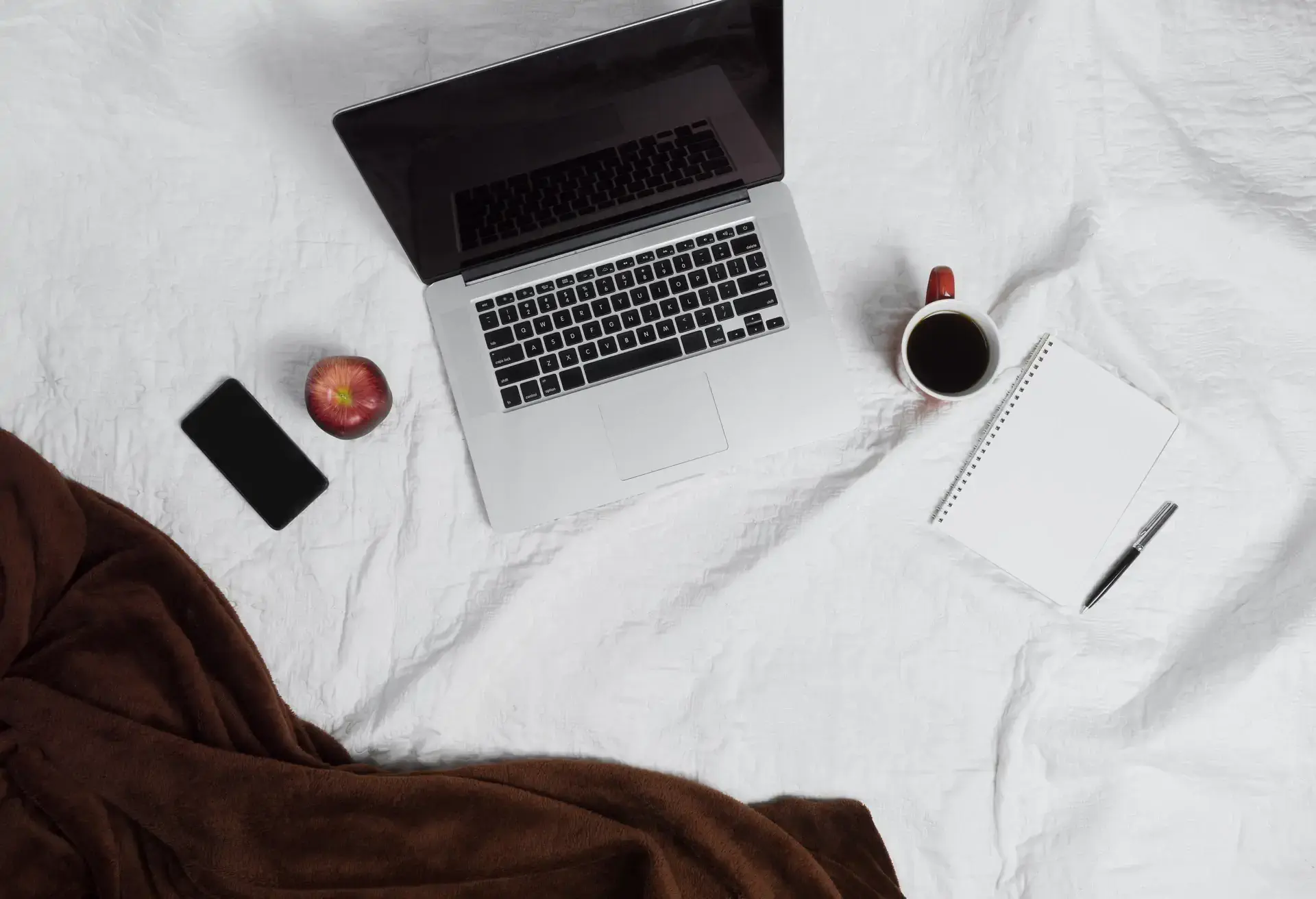 Laptop on the bad next to it an apple and a coffee mug