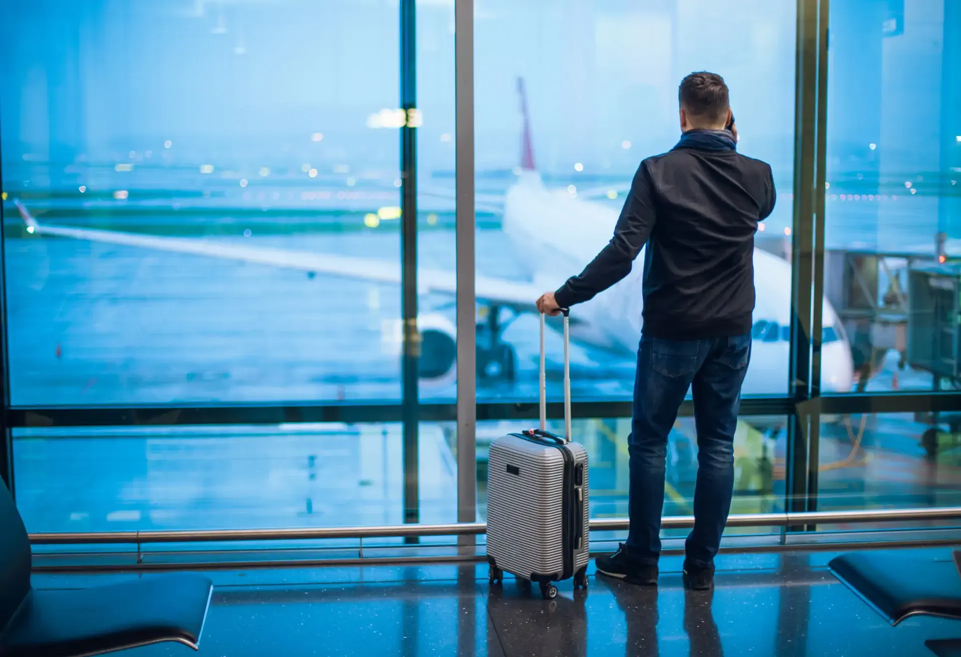 A man standing at the airport and looking through the window