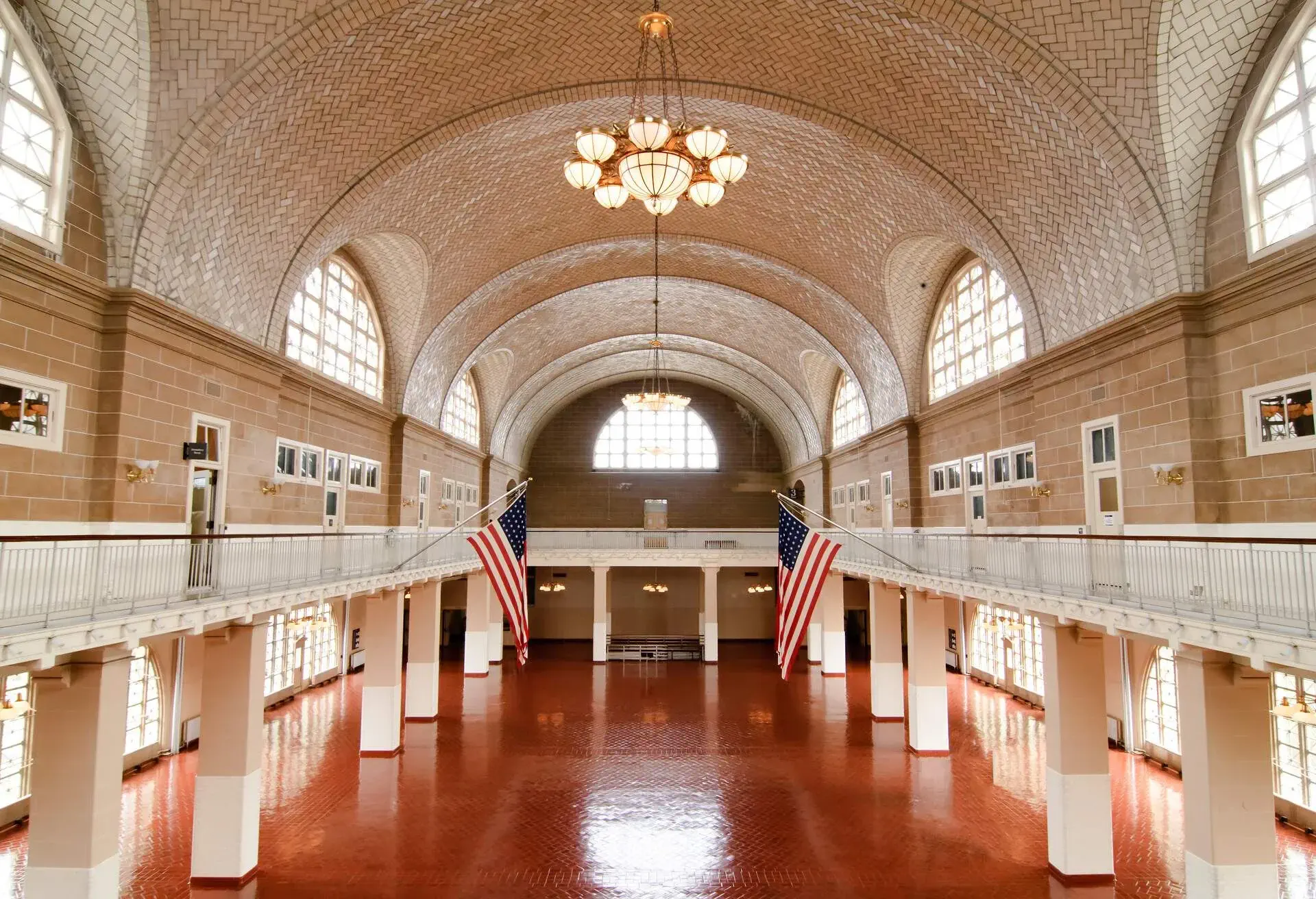 Interior of a building with a grand hallway with pillared balconies and arch ceilings with bright chandeliers.