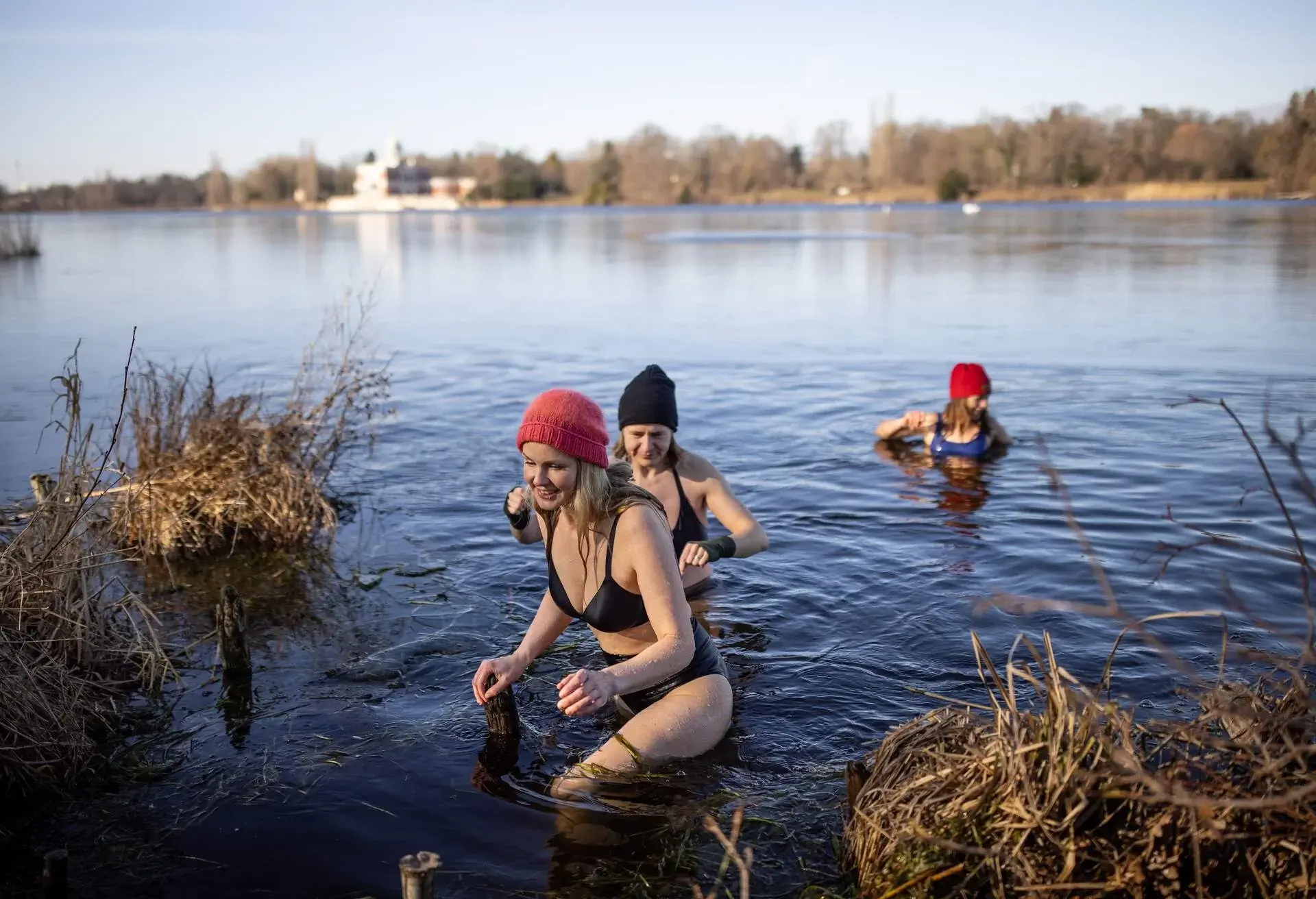 Three women in wooly hats bathing in a lake in winter on a sunny day