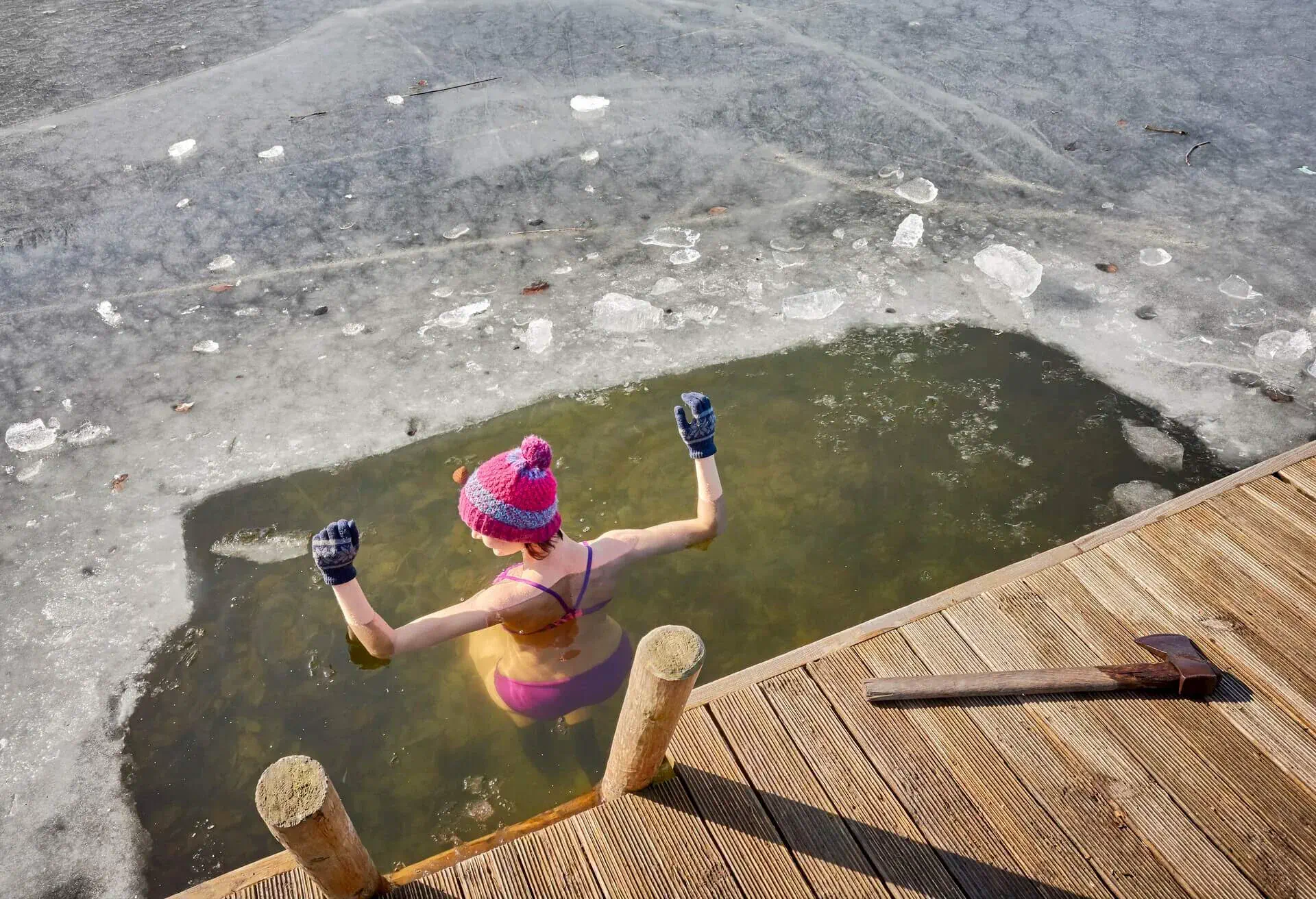 Woman in pink wool hat and gloves winter bathing in an ice pool on a frozen lake