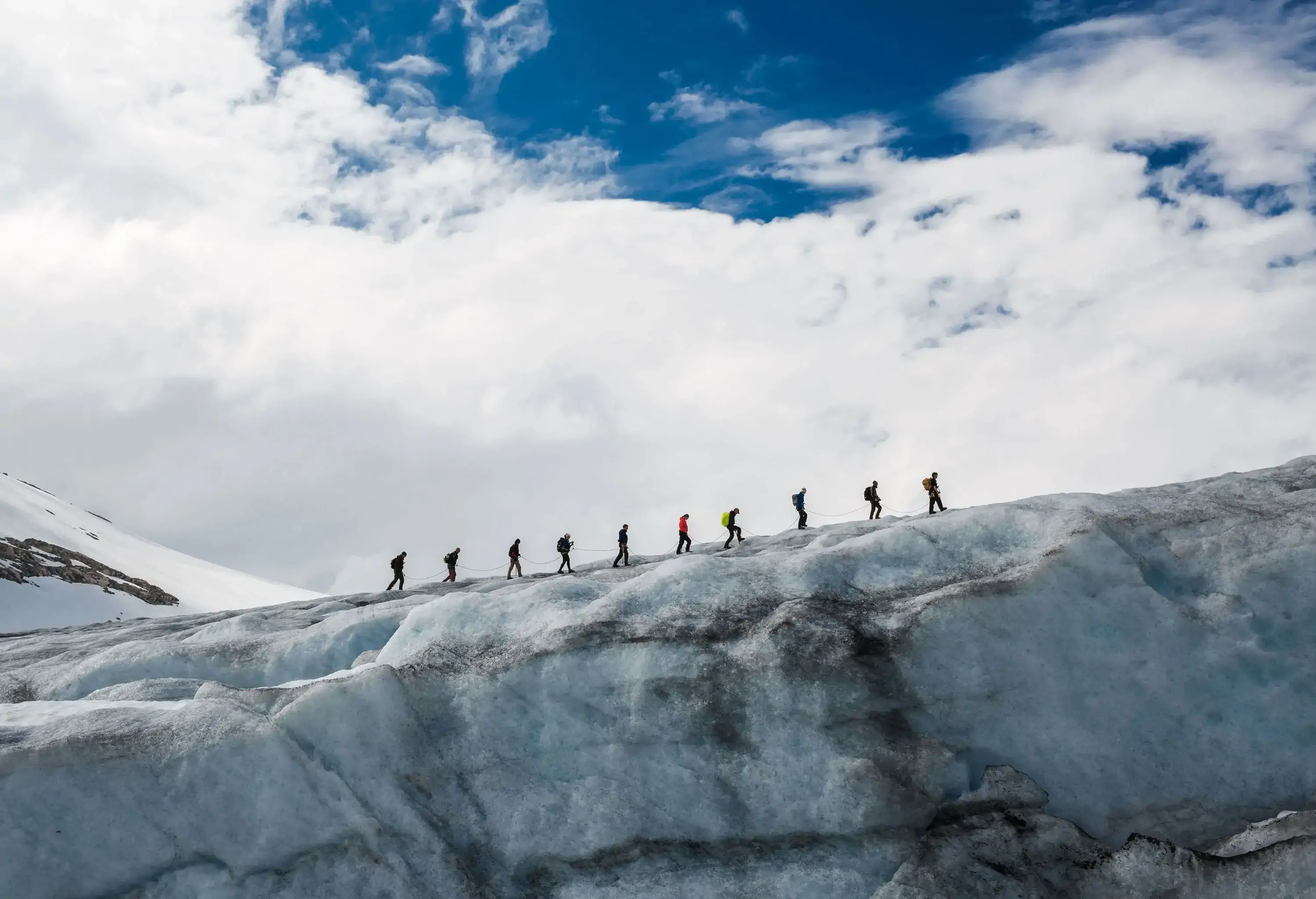 A group of hikers use a rope to walk in a line on top of a glacier.