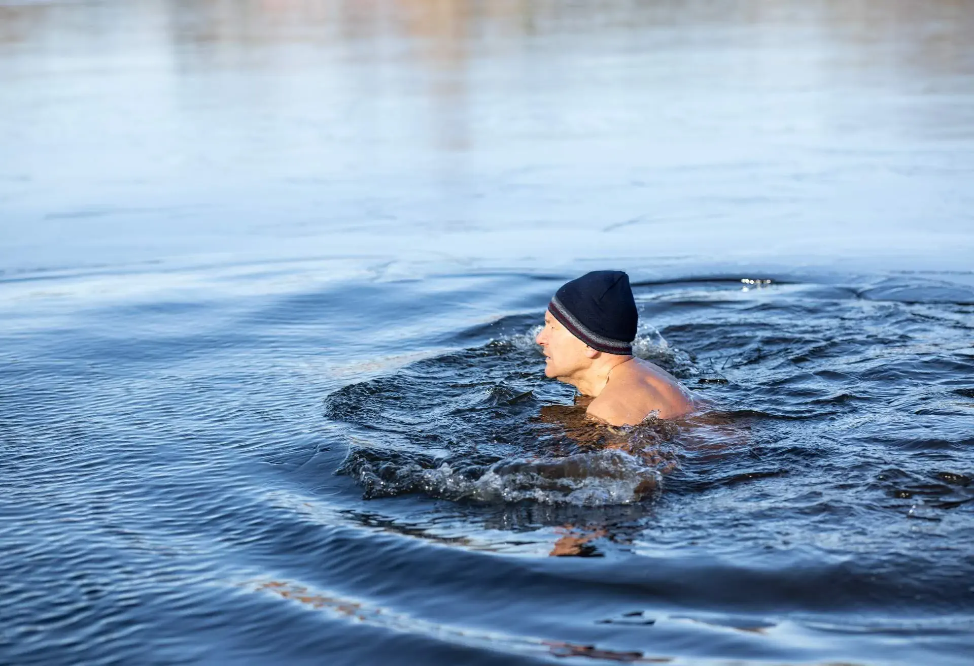 Man wearing a wool hat swimming in cold lake water in winter