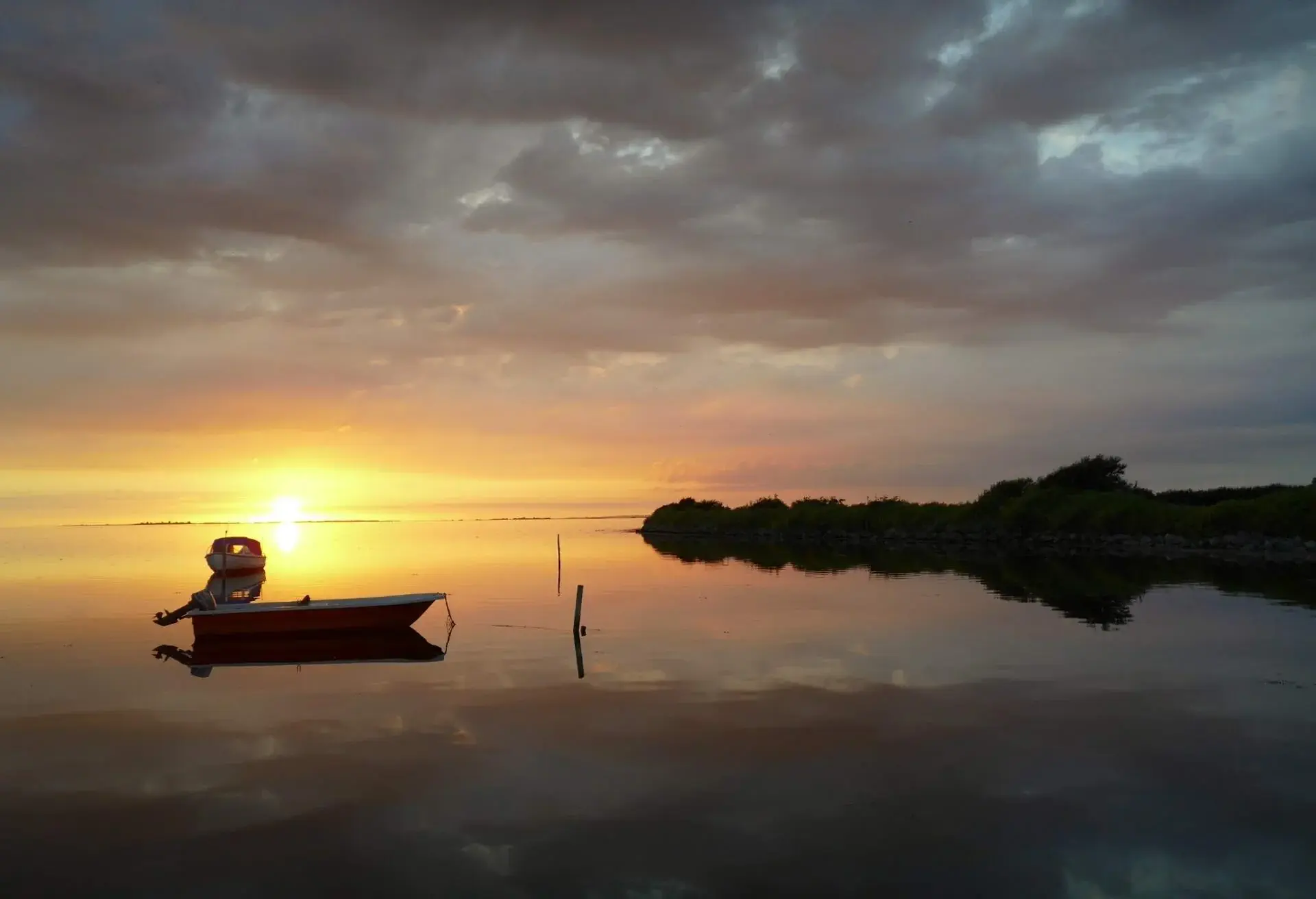 Sunset over a lake on a cloudy winter day, with one boat reflected in the calm water