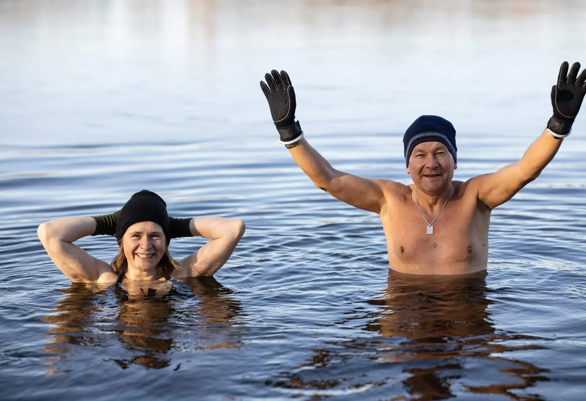 Man and woman wearing hat and gloves winter swimming in cold water