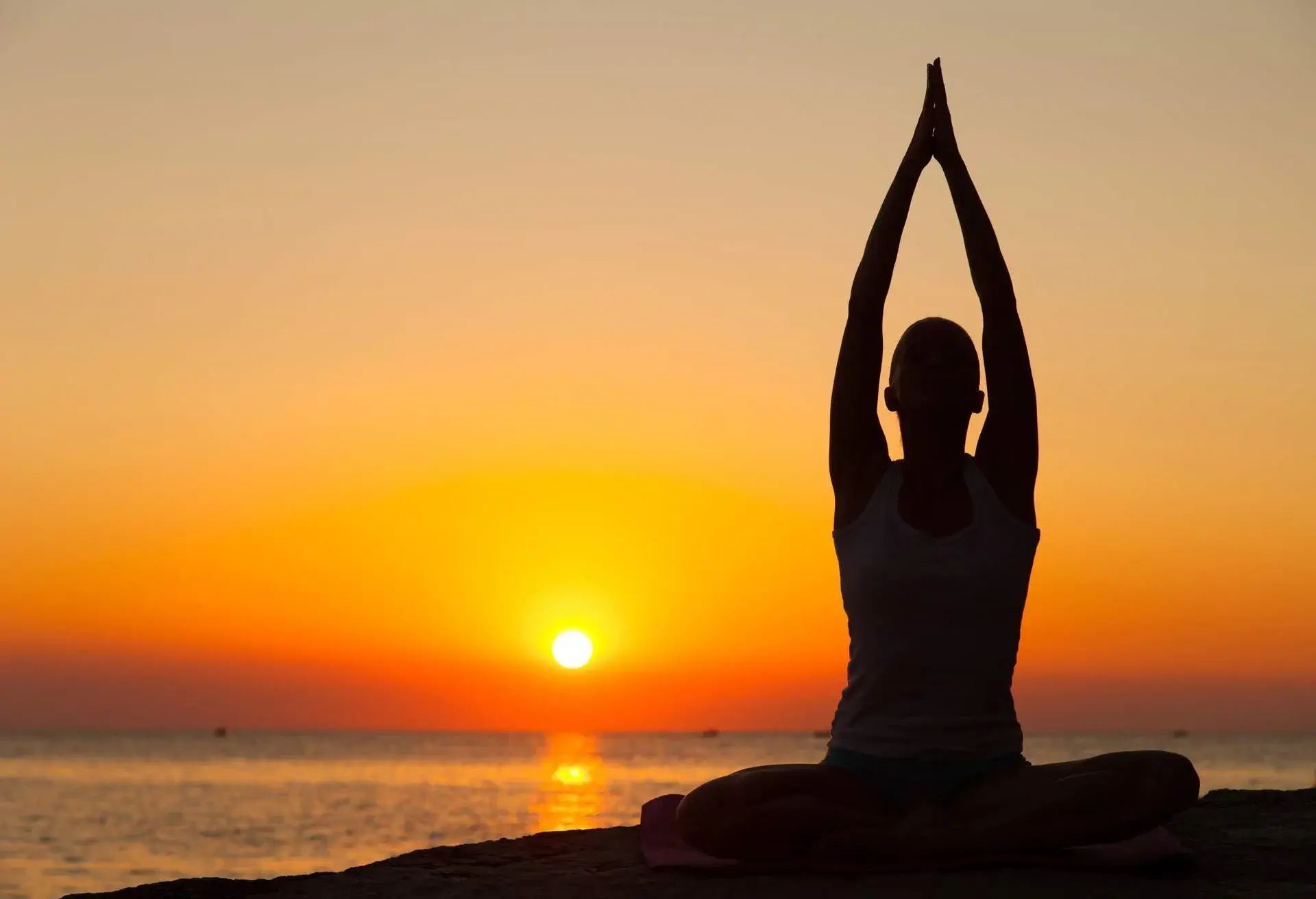 Silhouette of man doing sitting yoga at sunrise by the beach