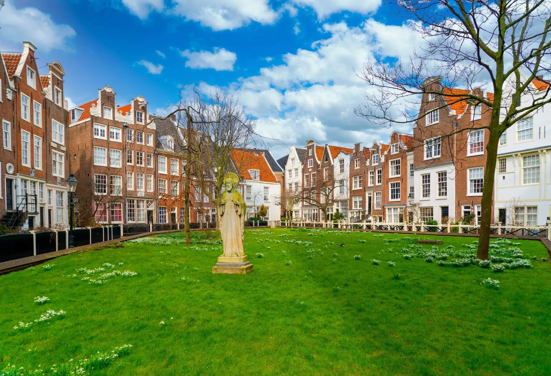 A park in Amsterdam surrounded by iconic narrow buildings and a statue in the middle on the grass