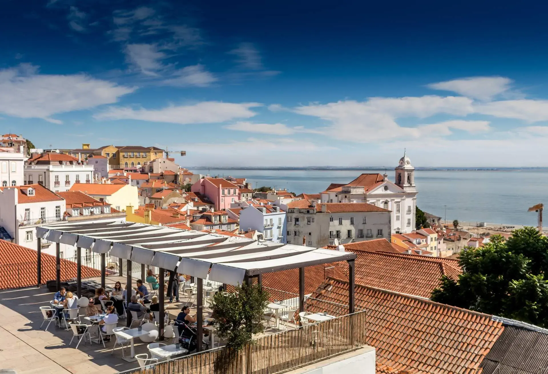 People dining on a terrace overlooking the city rooftops and the sea.