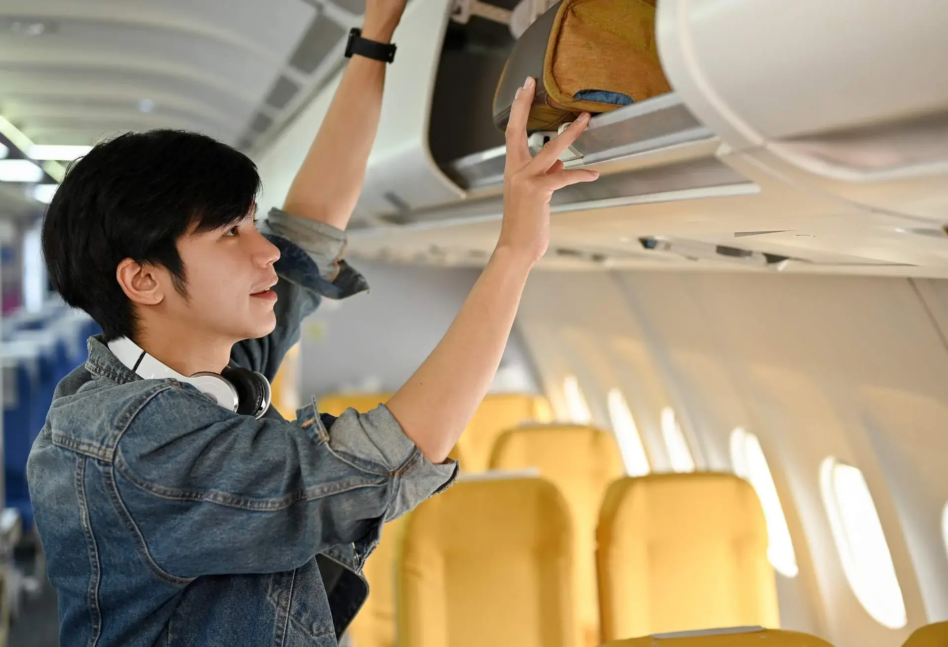 A man placing his cabin bag into an overhead bin