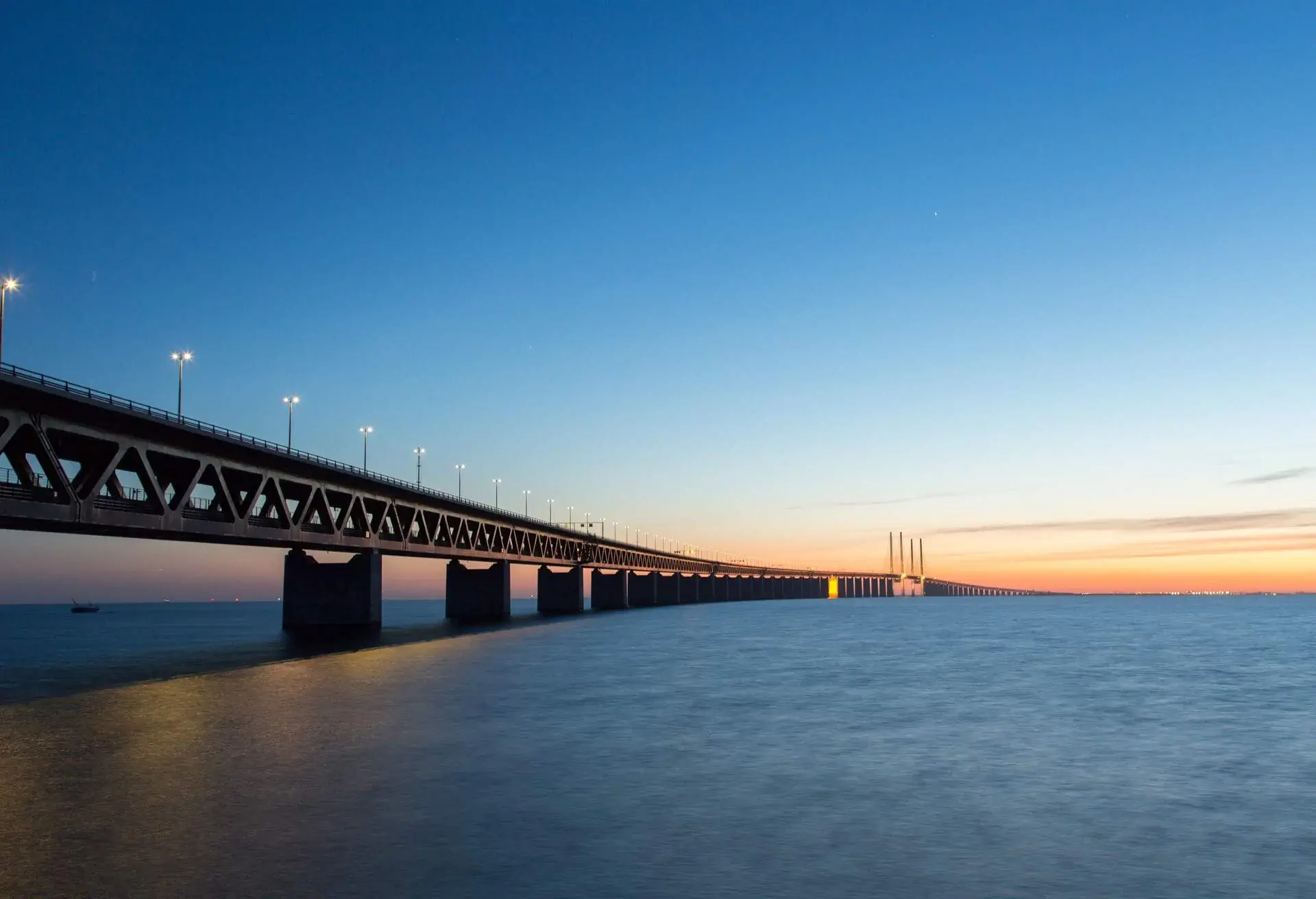 A large body of water with a long bridge lit by lampposts.
