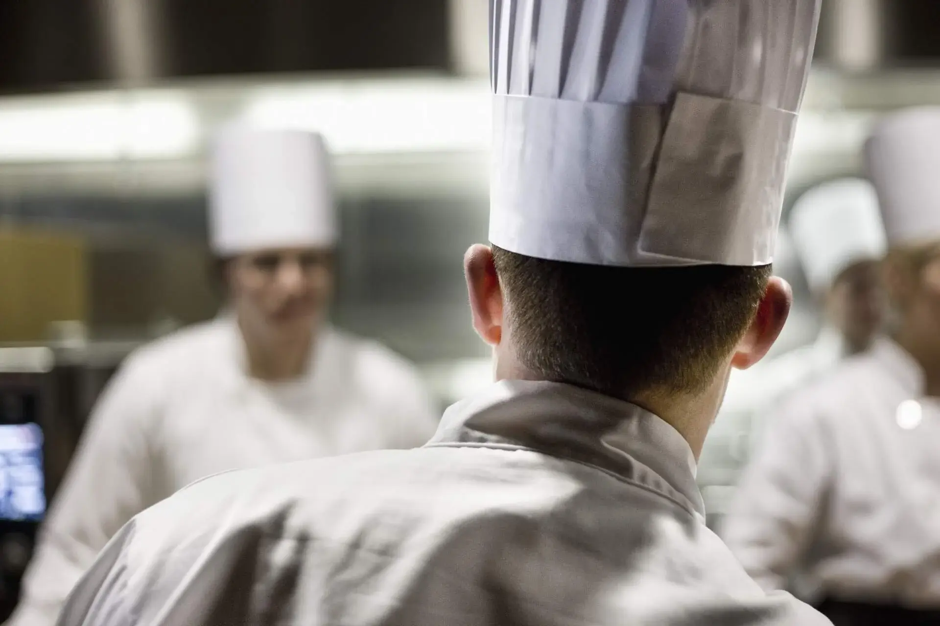 Group of chefs wearing toque hats inside a kitchen.
