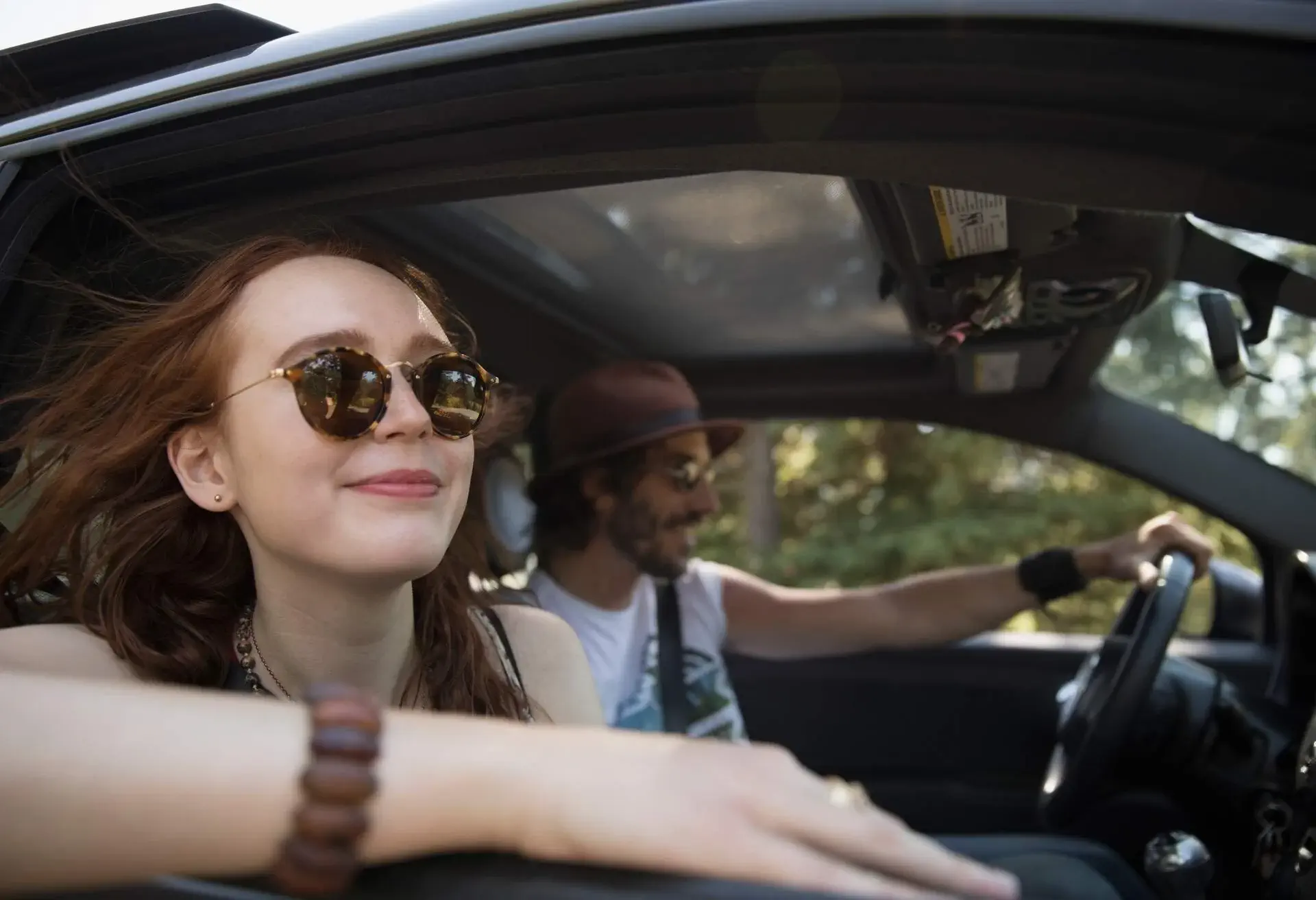 A couple in a car, the man is driving, the woman looks outside the window