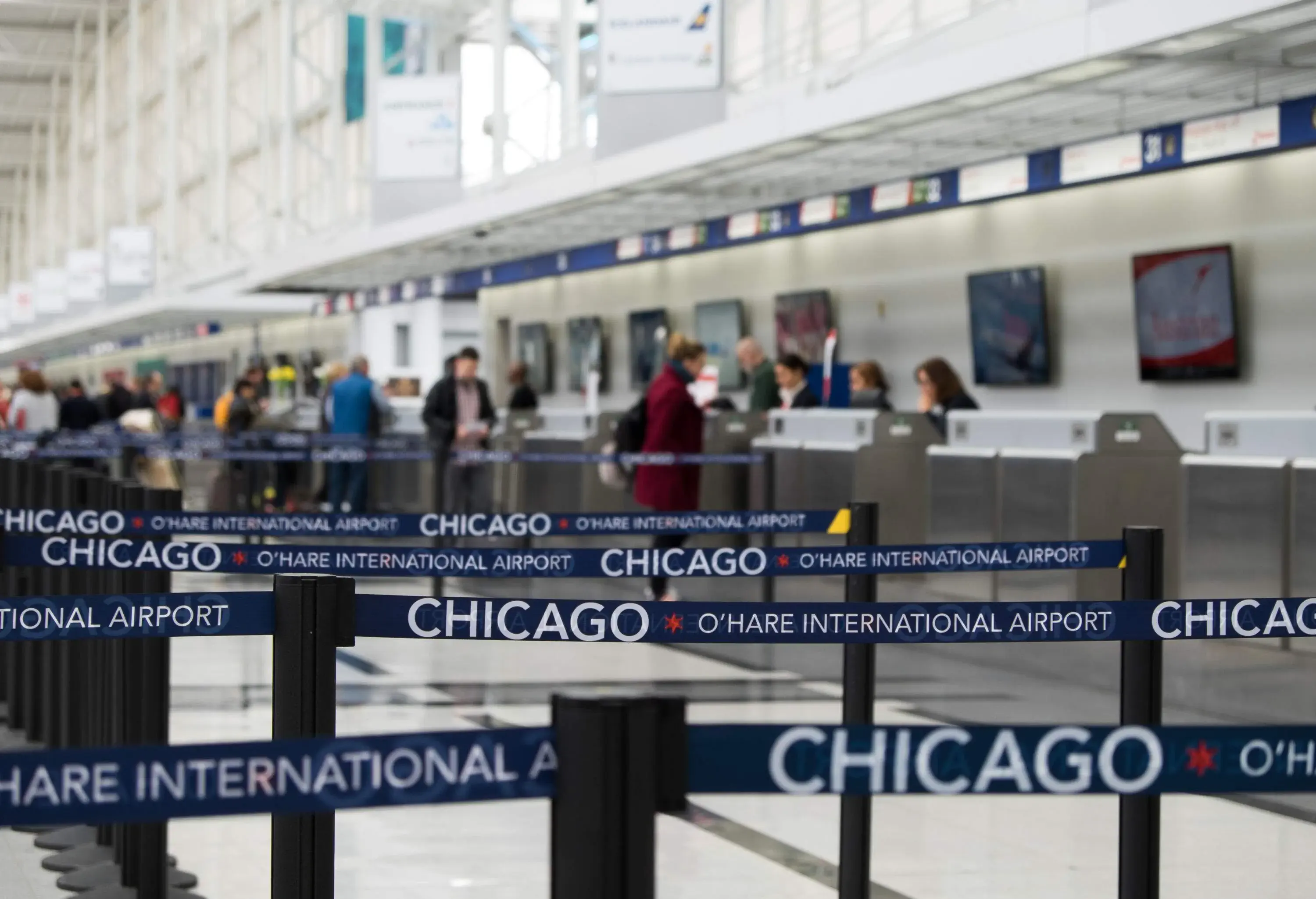 Focused image of a belt line with text that reads "Chicago O'Hare International Airport" against the bokeh background of people in the check-in counter.