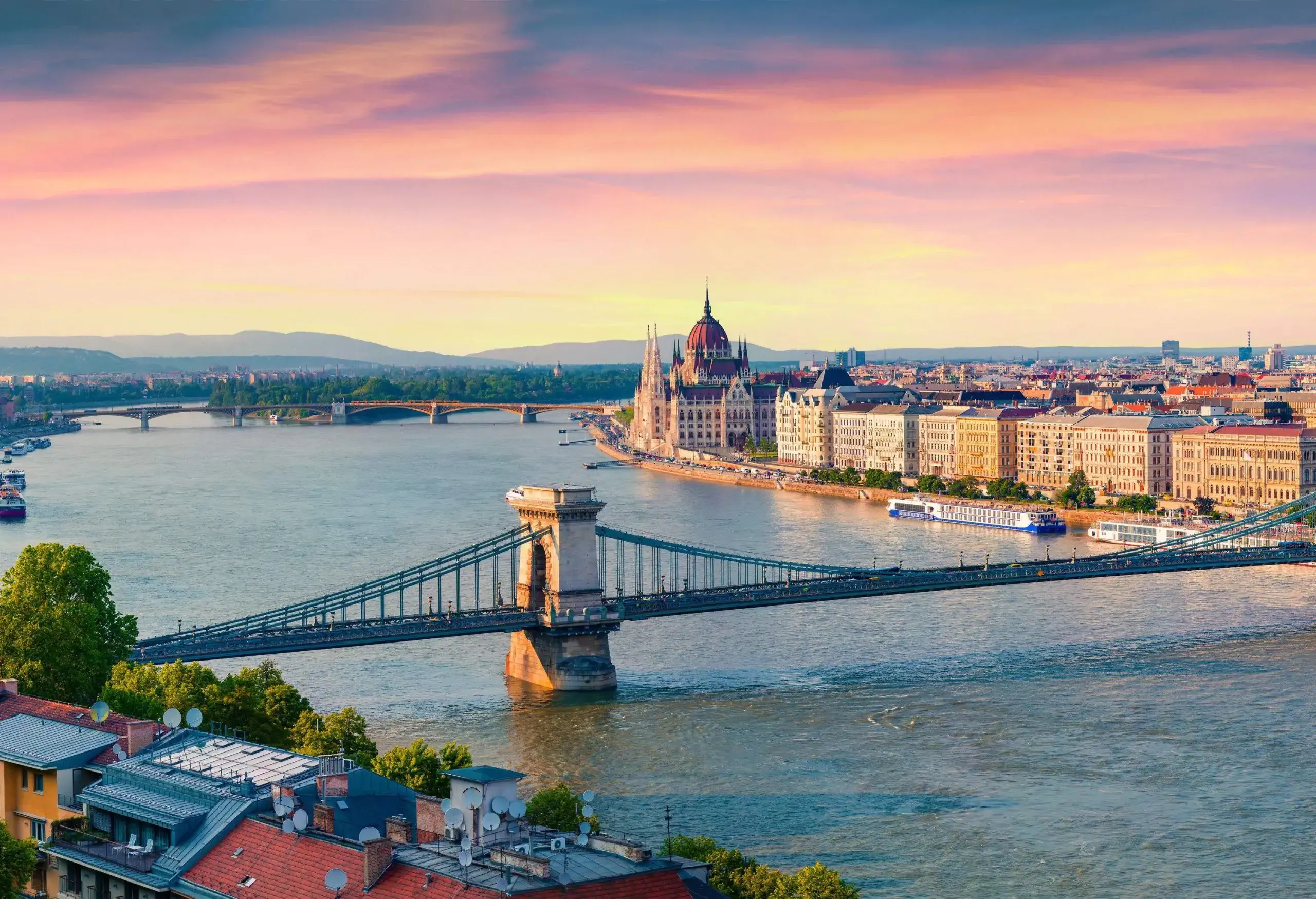 A suspension bridge across a river with views of a cityscape.
