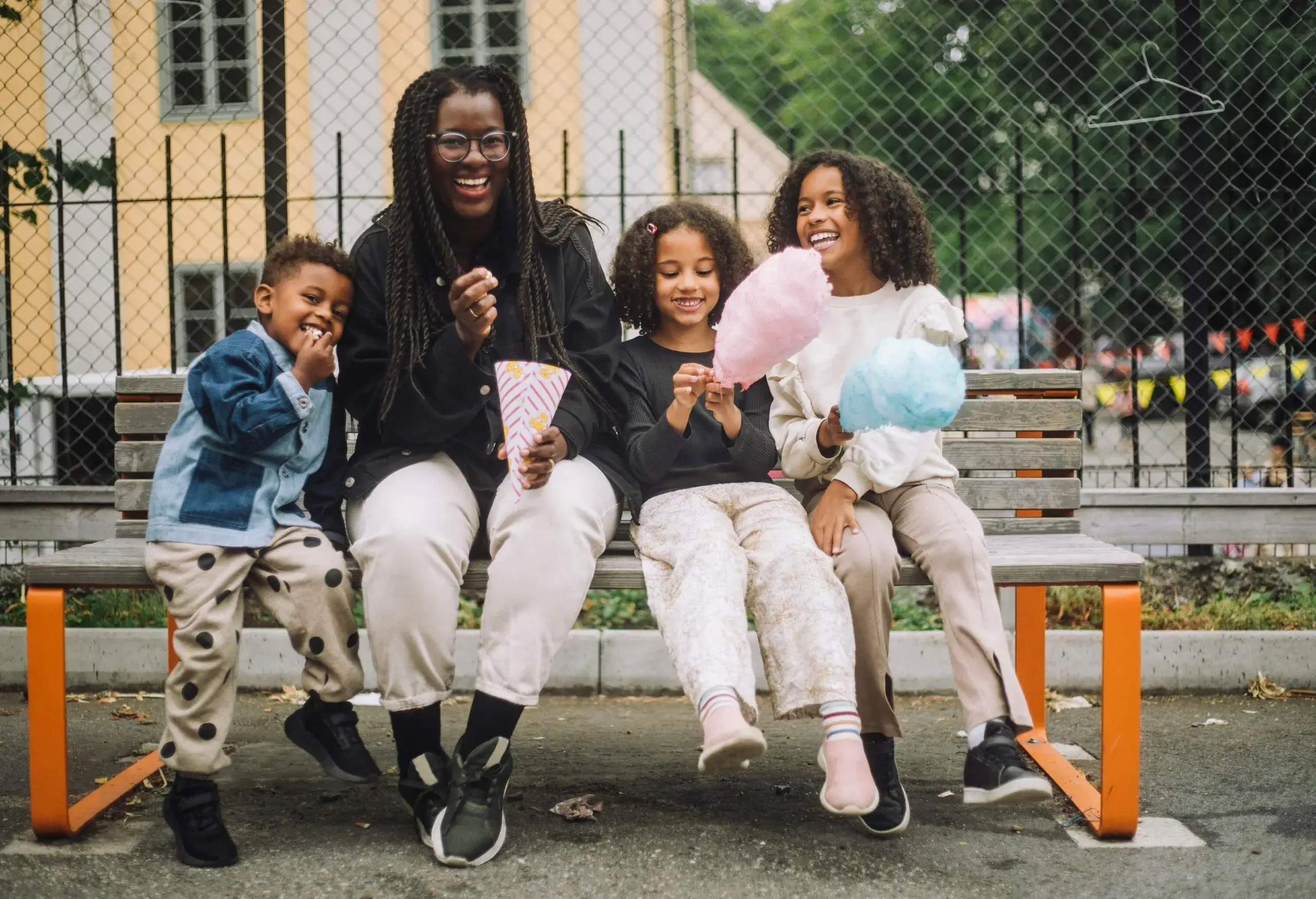 a woman sitting with three kids on a bench in a park and eating candy