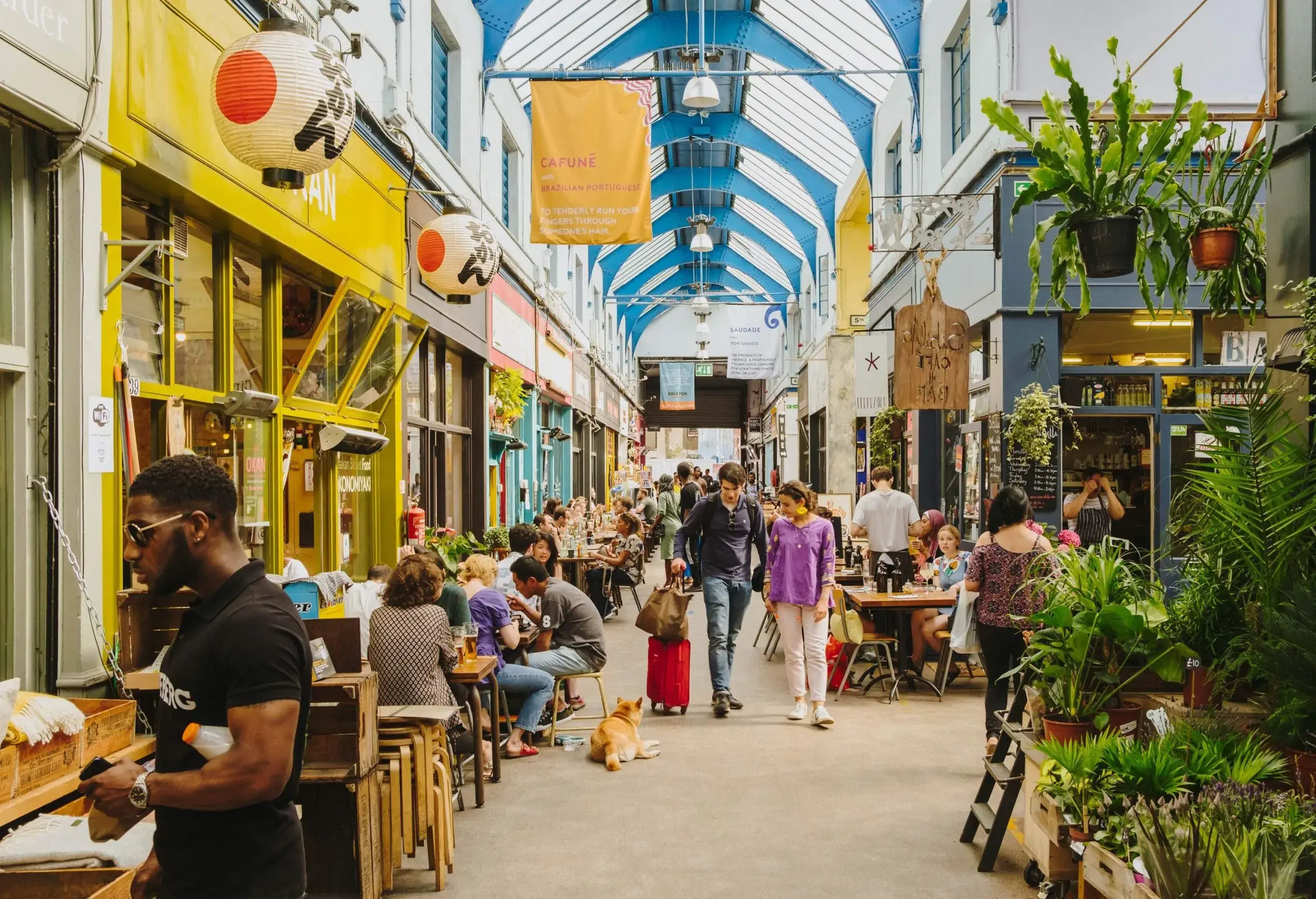 A woman and a man with luggage walking through a market gallery, pausing to see a dog laying on the floor.