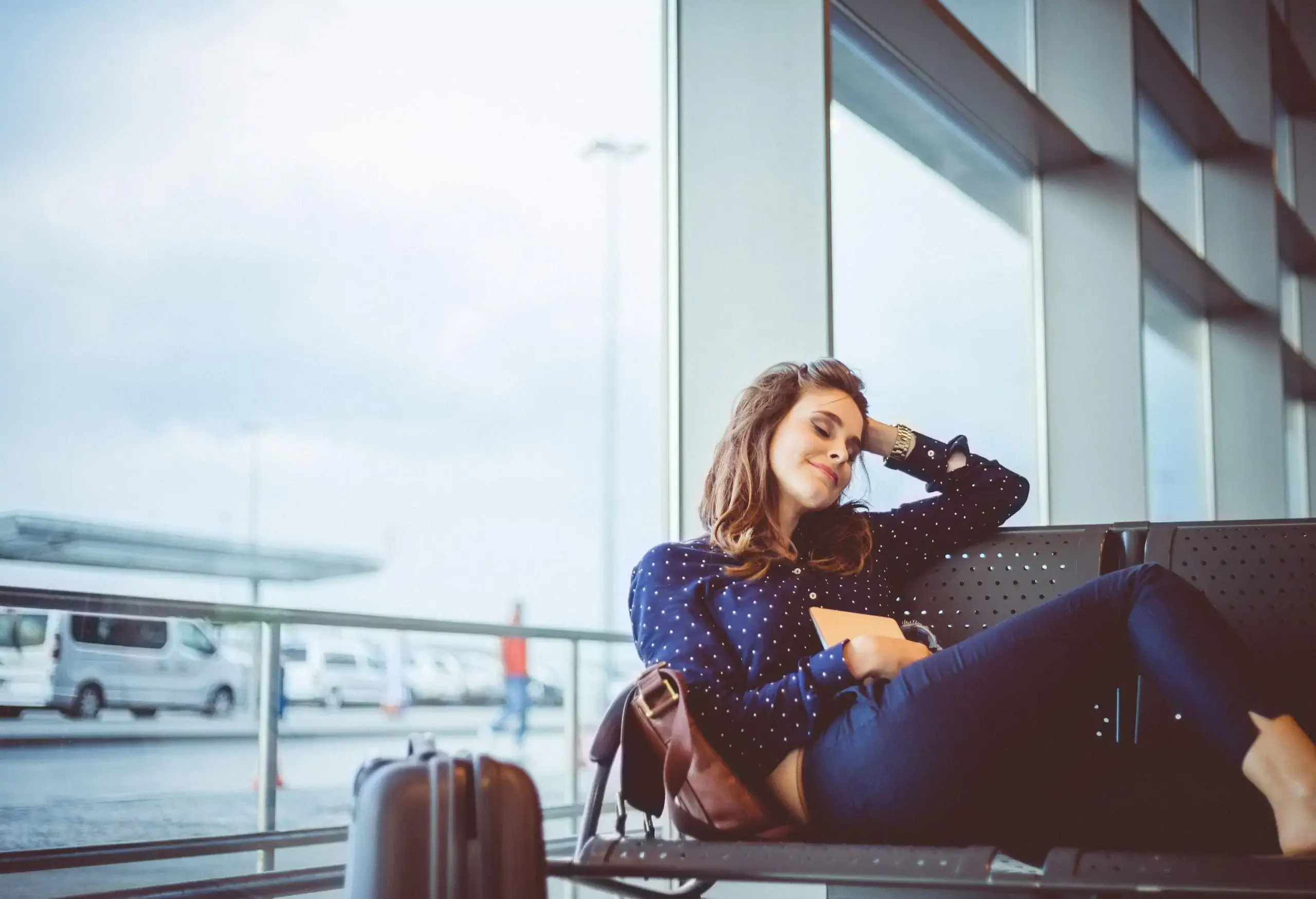 A female passenger waiting happily at a terminal as she sits comfortably in a row of chairs.