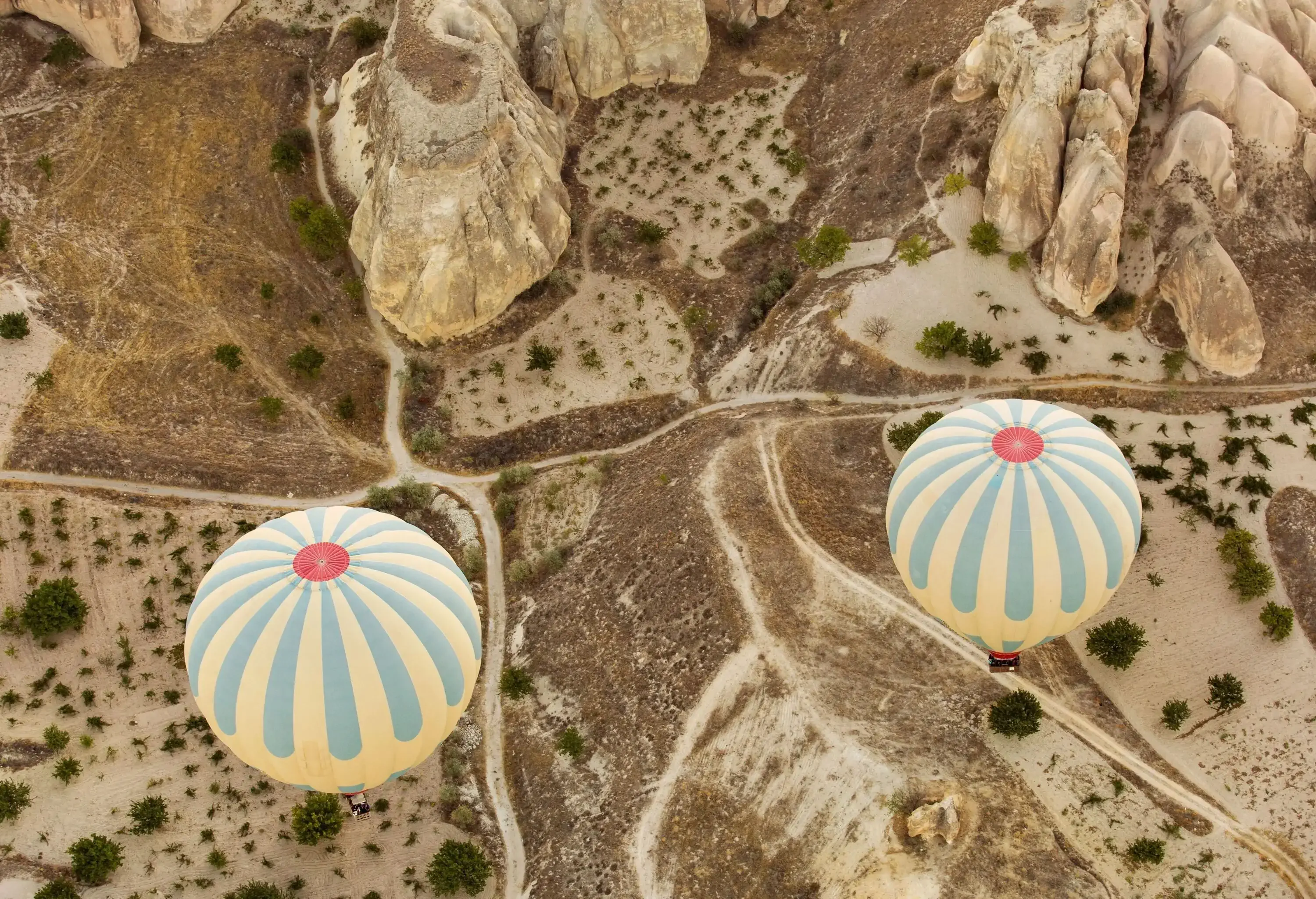 Two colourful hot air balloons flying over a terrain of volcanic mountains.