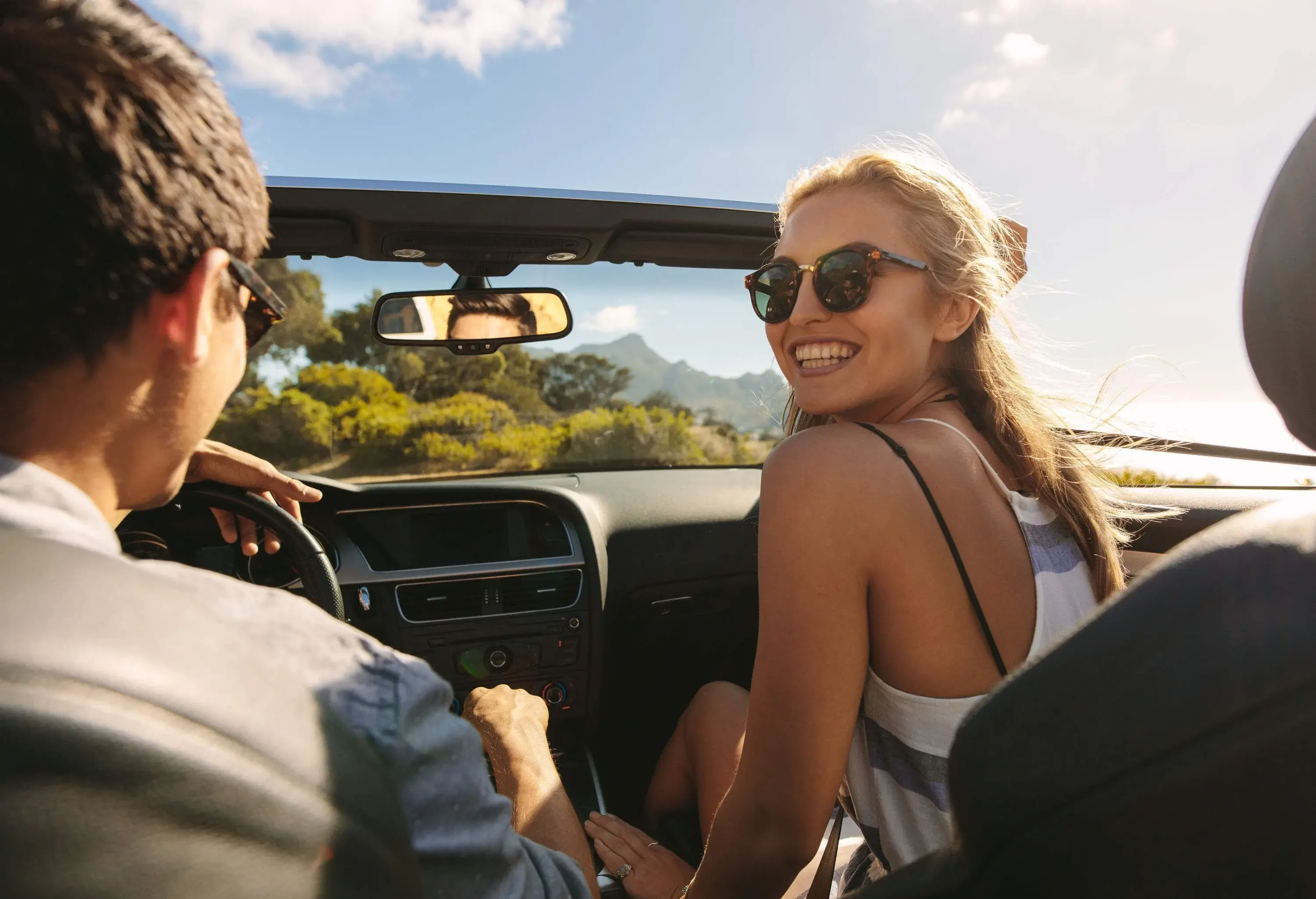 A young lady sitting in the passenger seat as the man takes them on the road in a convertible car.