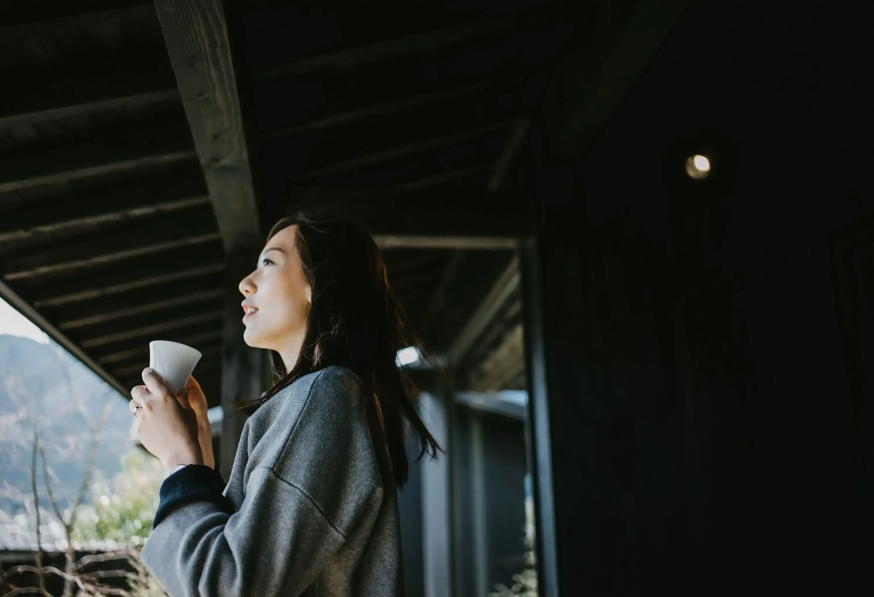 Beautiful young Asian woman drinking coffee and relaxing on balcony on a fresh bright morning