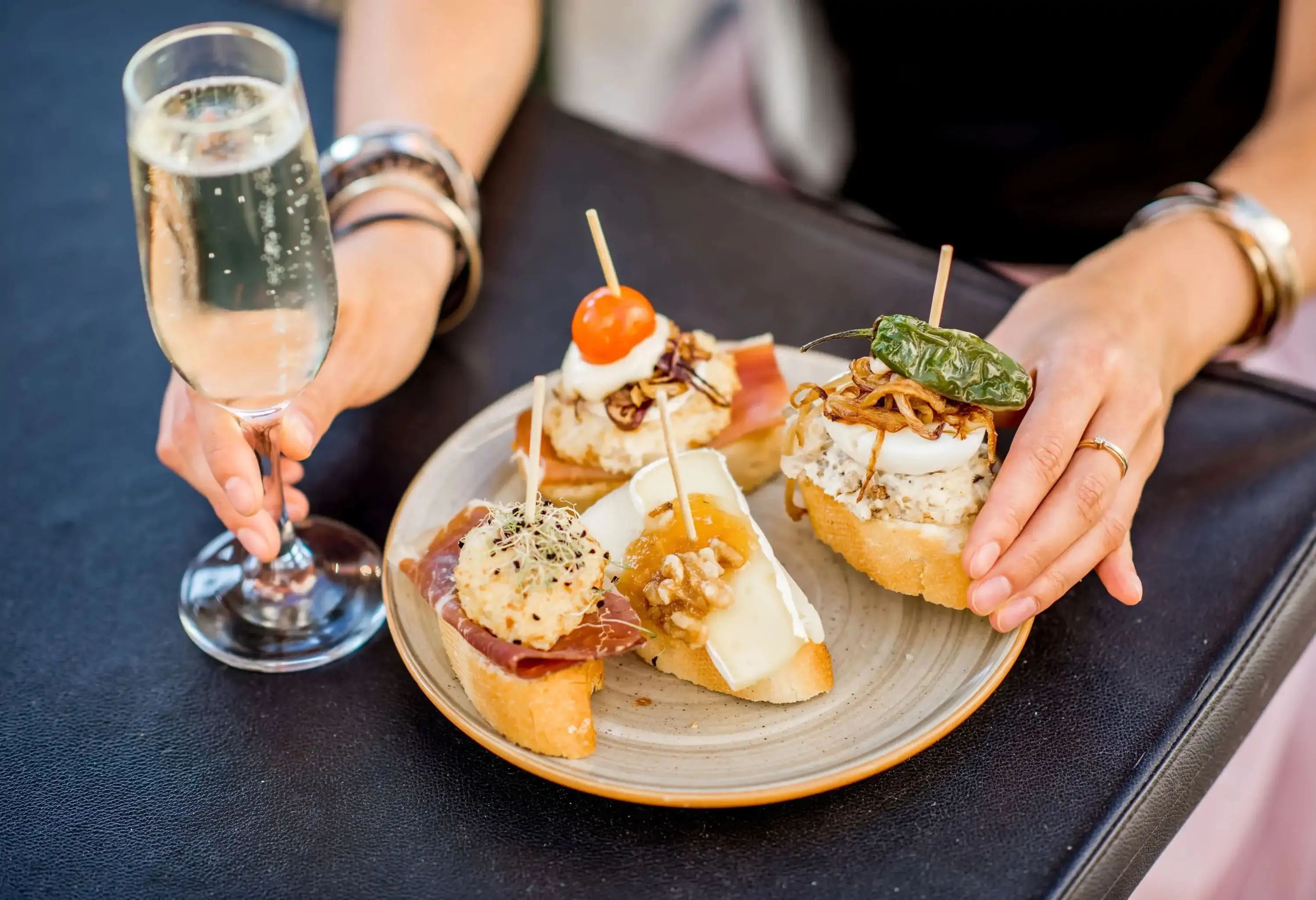 A vibrant and enticing display of pinchos, showcasing an array of beautiful and colourful bite-sized treats, with a person delicately holding one piece in hand, complemented by a glass of wine.