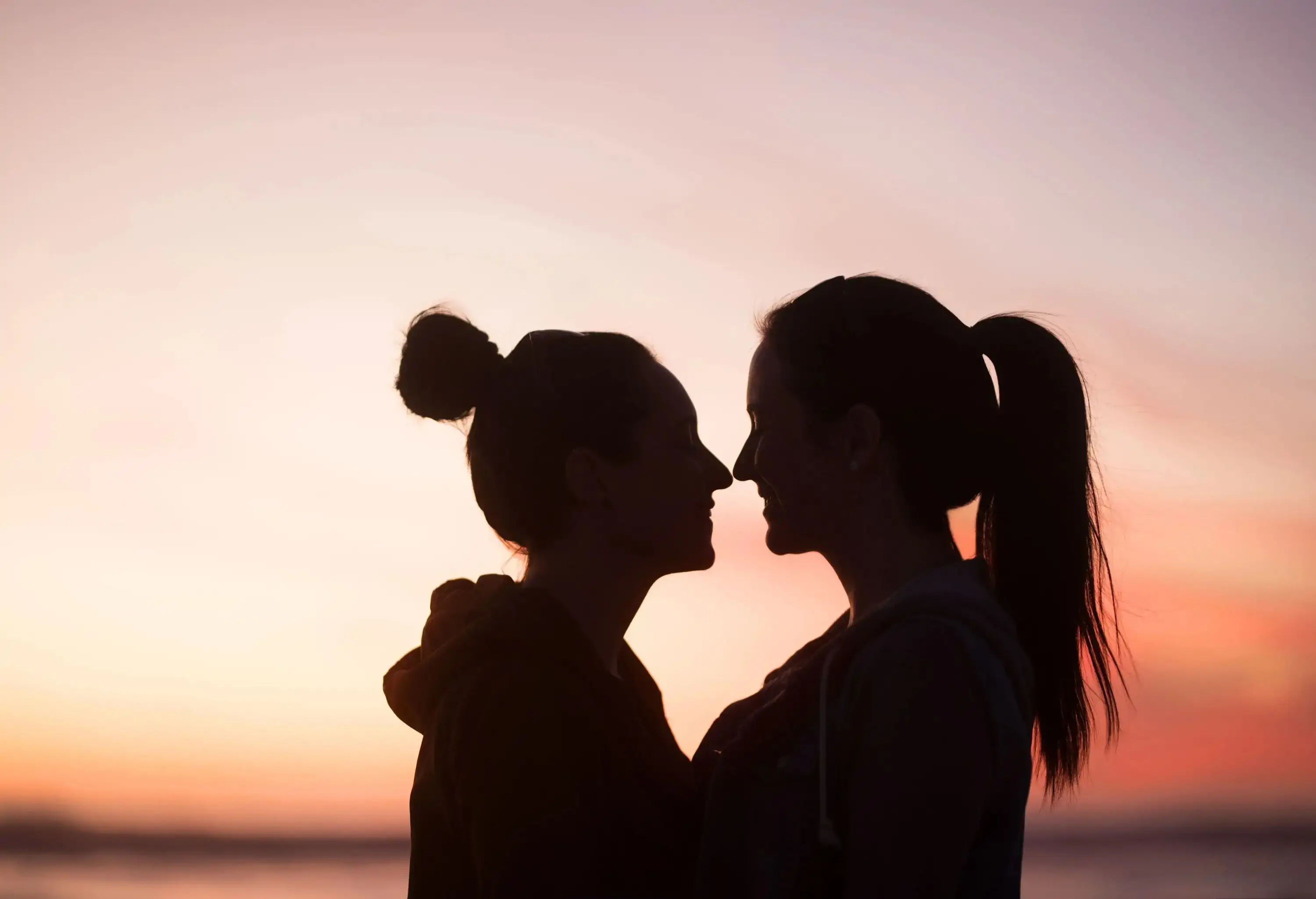 Two women standing face to face and smiling at each other at dusk.