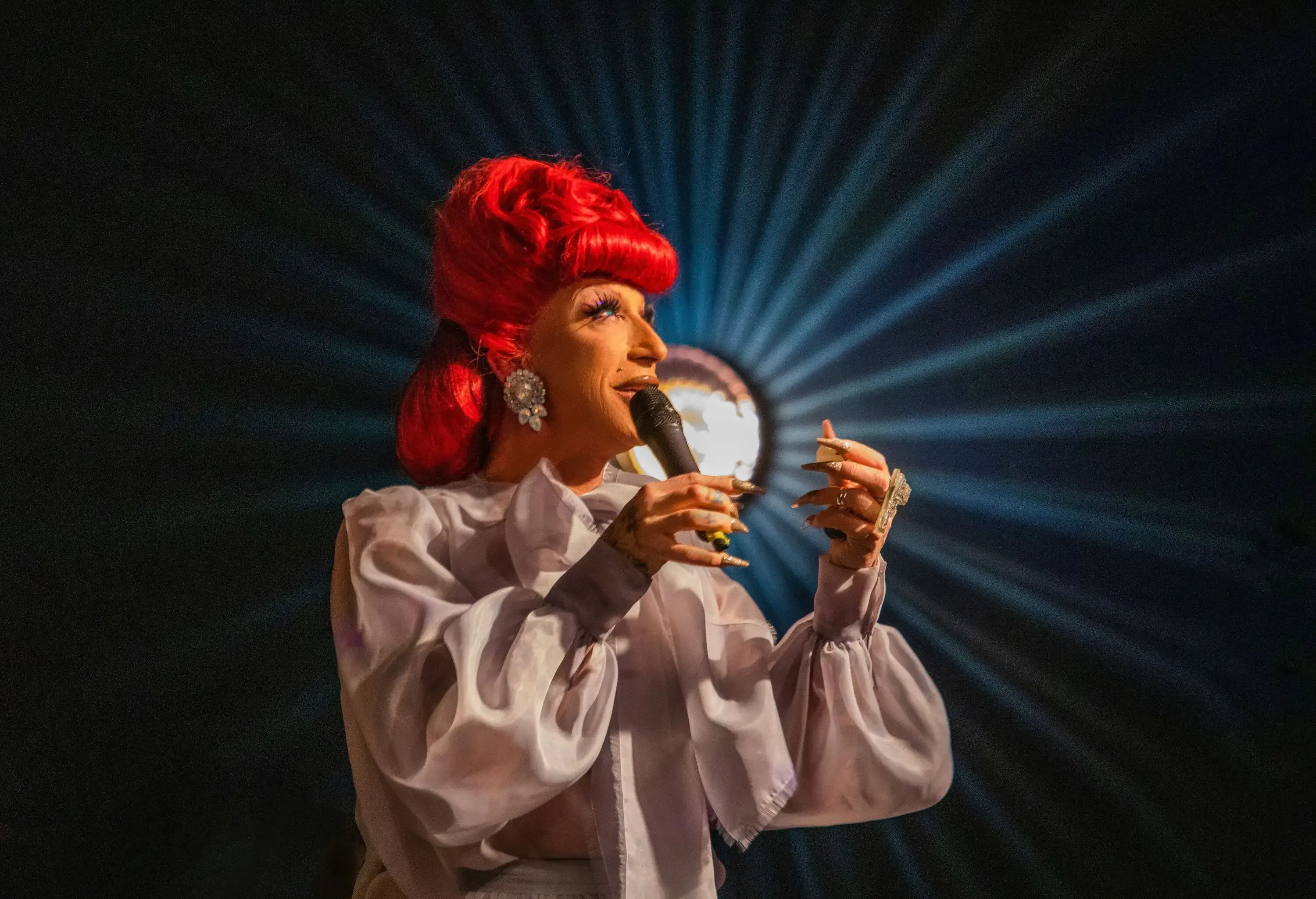 A performer dressed in drag and wearing a red wig.