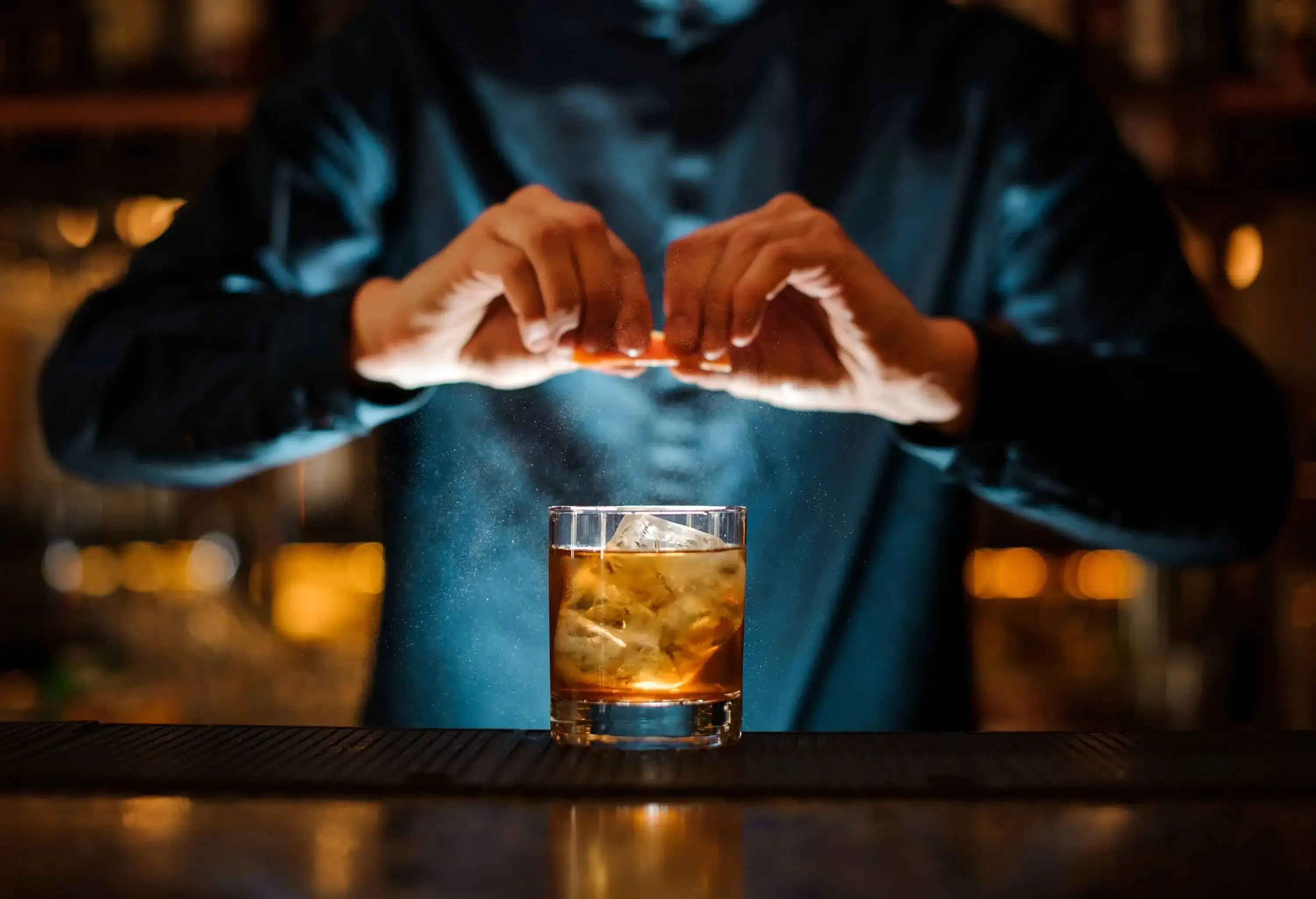 A bartender squeezes an orange over a glass of cocktail drink.