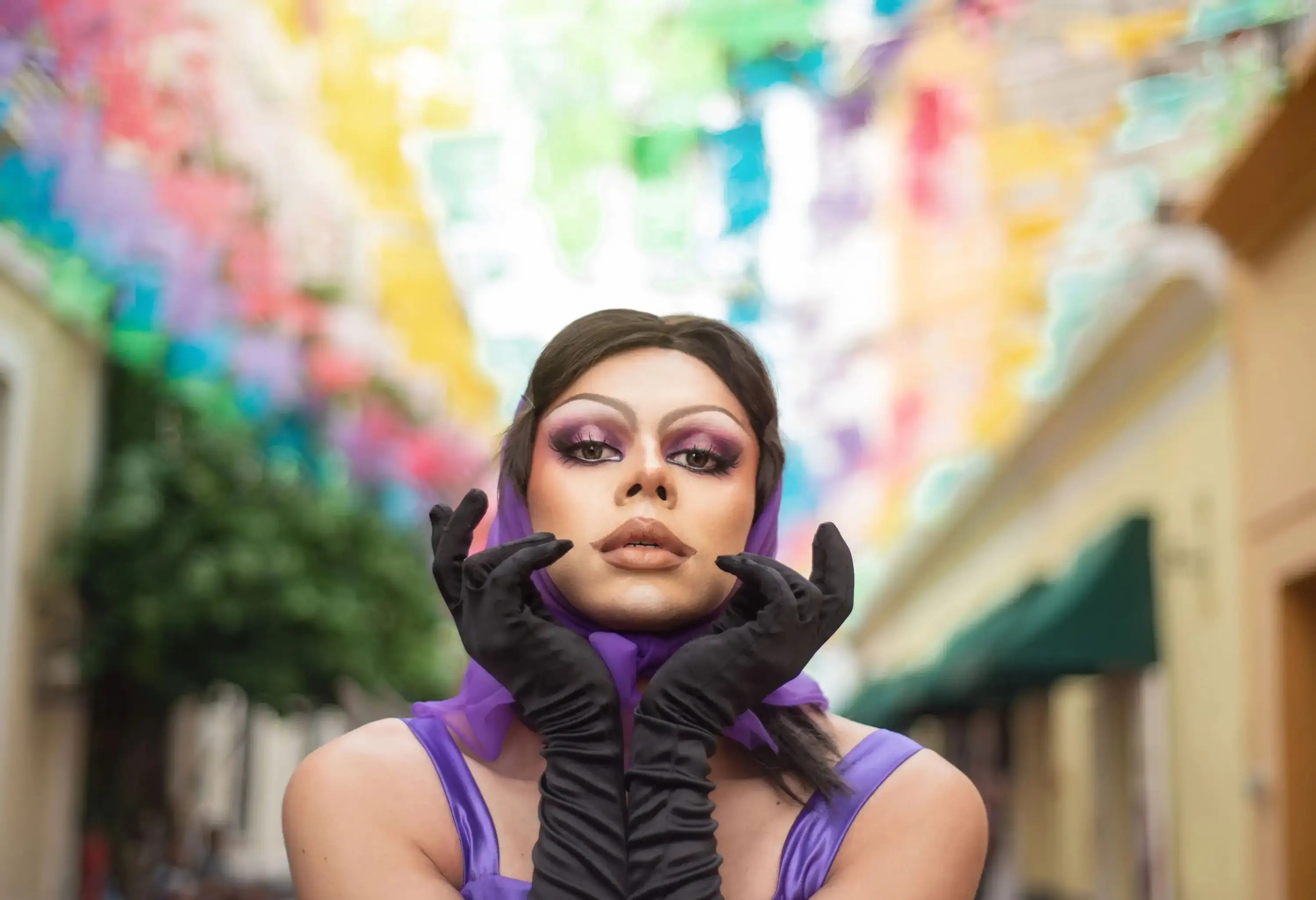 Drag Queen street portrait with multicolor background. Young man dressed as a woman looking at the camera.