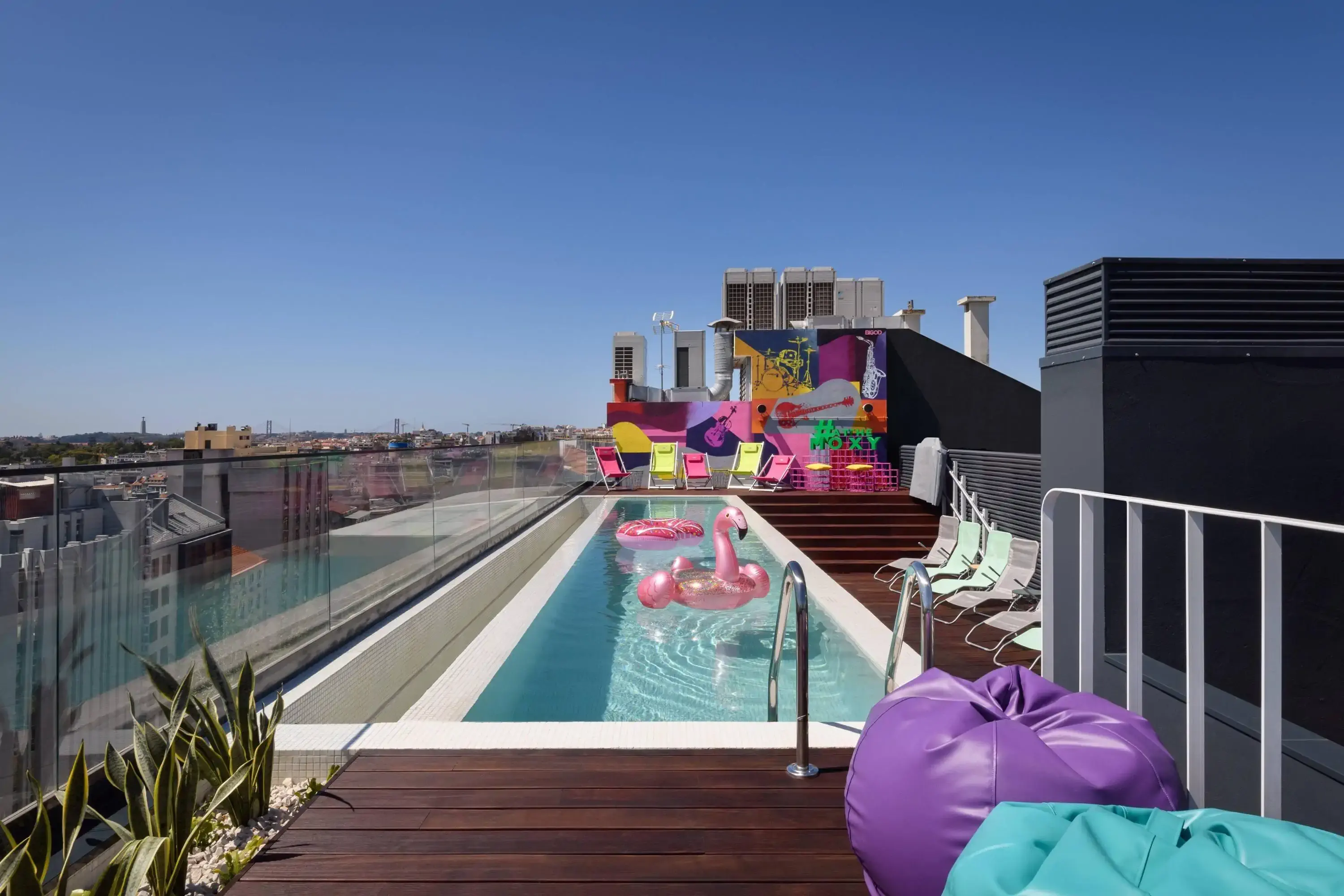 a rooftop pool with colorful sunbeds and a pink flamingo float