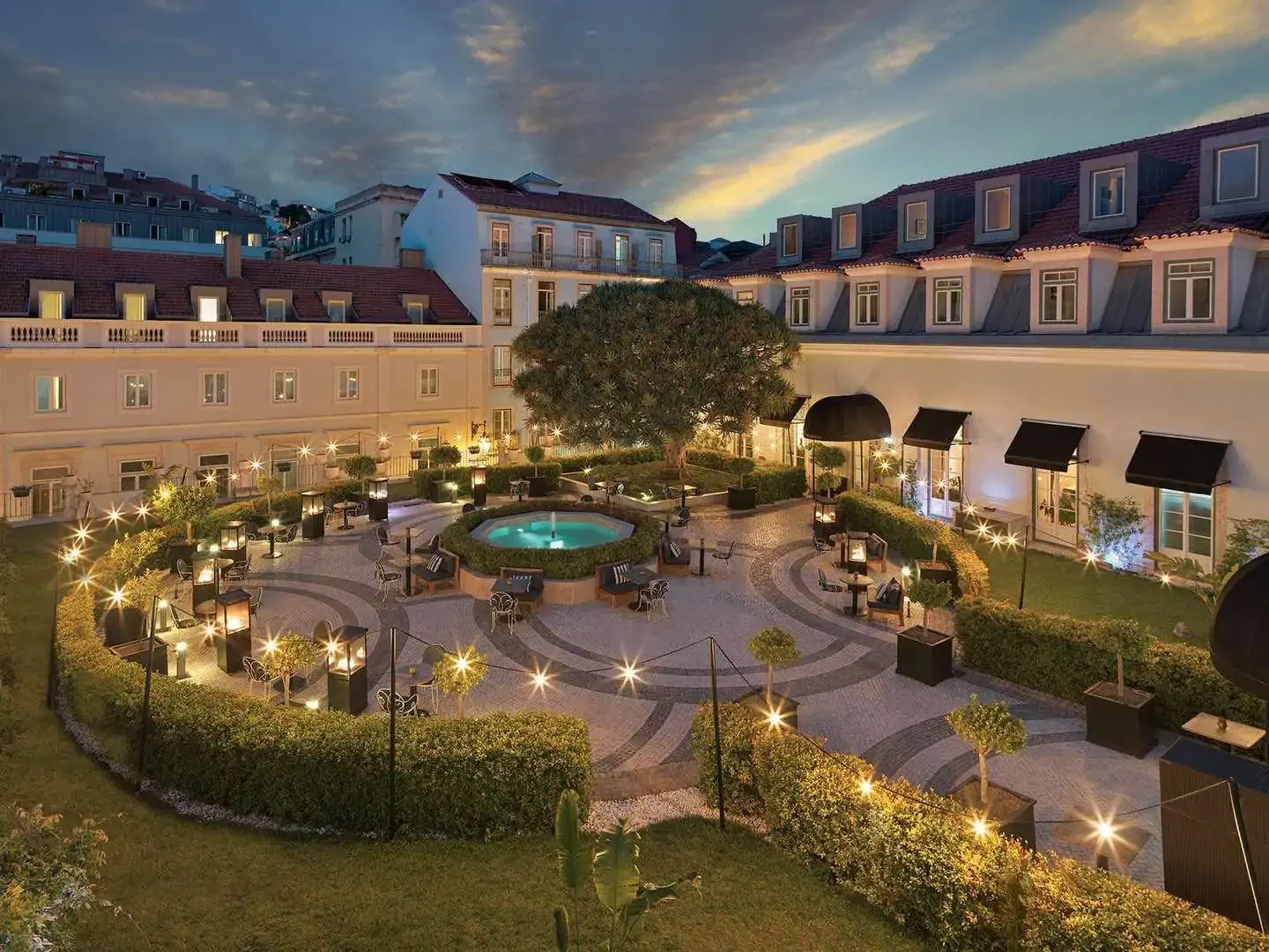 A luxurious courtyard at dusk, featuring a central fountain, elegant outdoor seating, and warm ambient lighting.