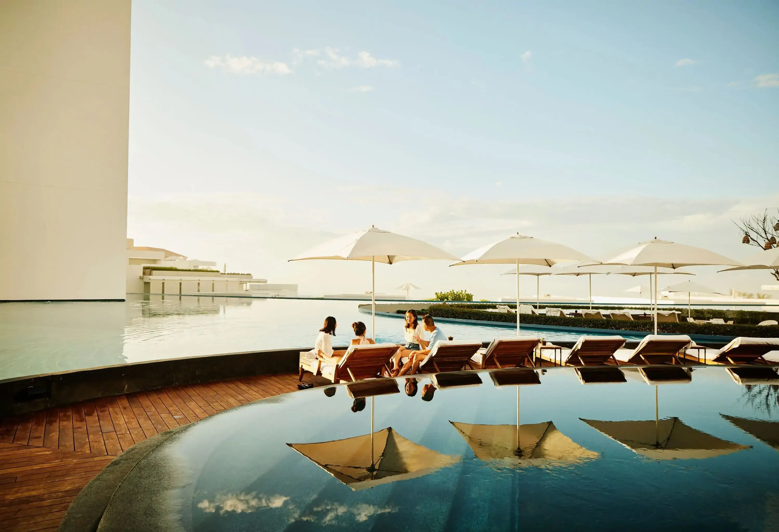 Extreme wide shot of family hanging out on lounge chairs by pool at tropical resort during vacation