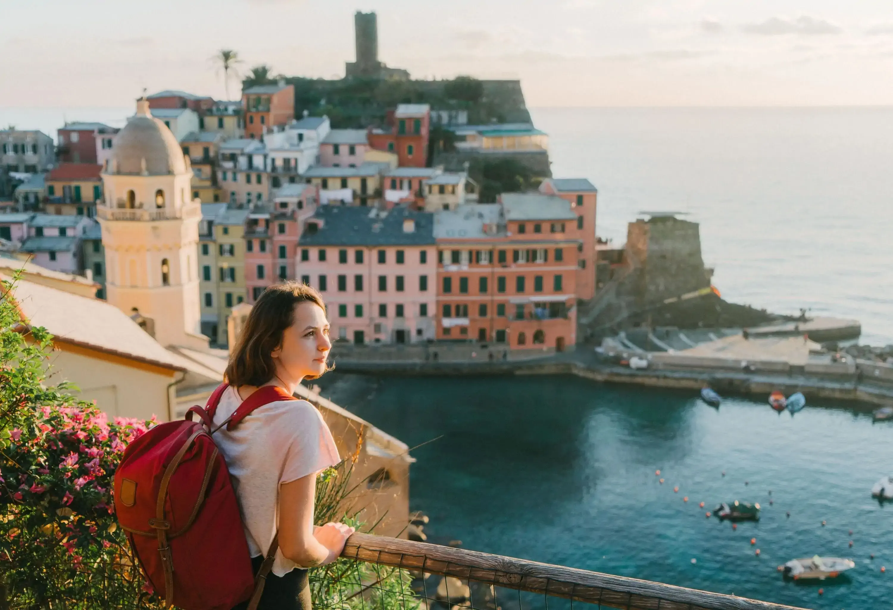 A young woman with a backpack standing on a bridge, taking in the sights of a coastal town.