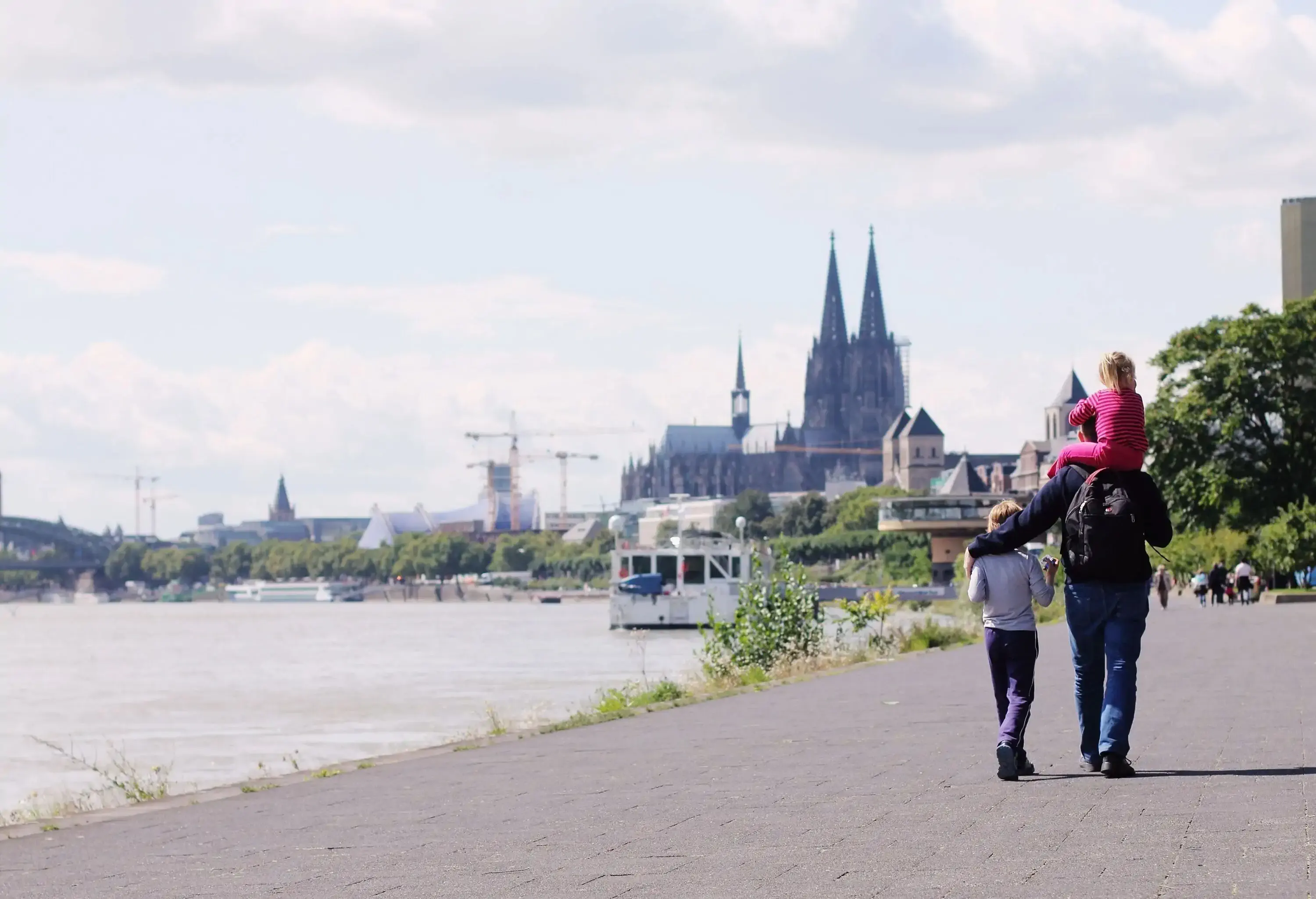 A father and his two kids walk on the promenade alongside the broad river.
