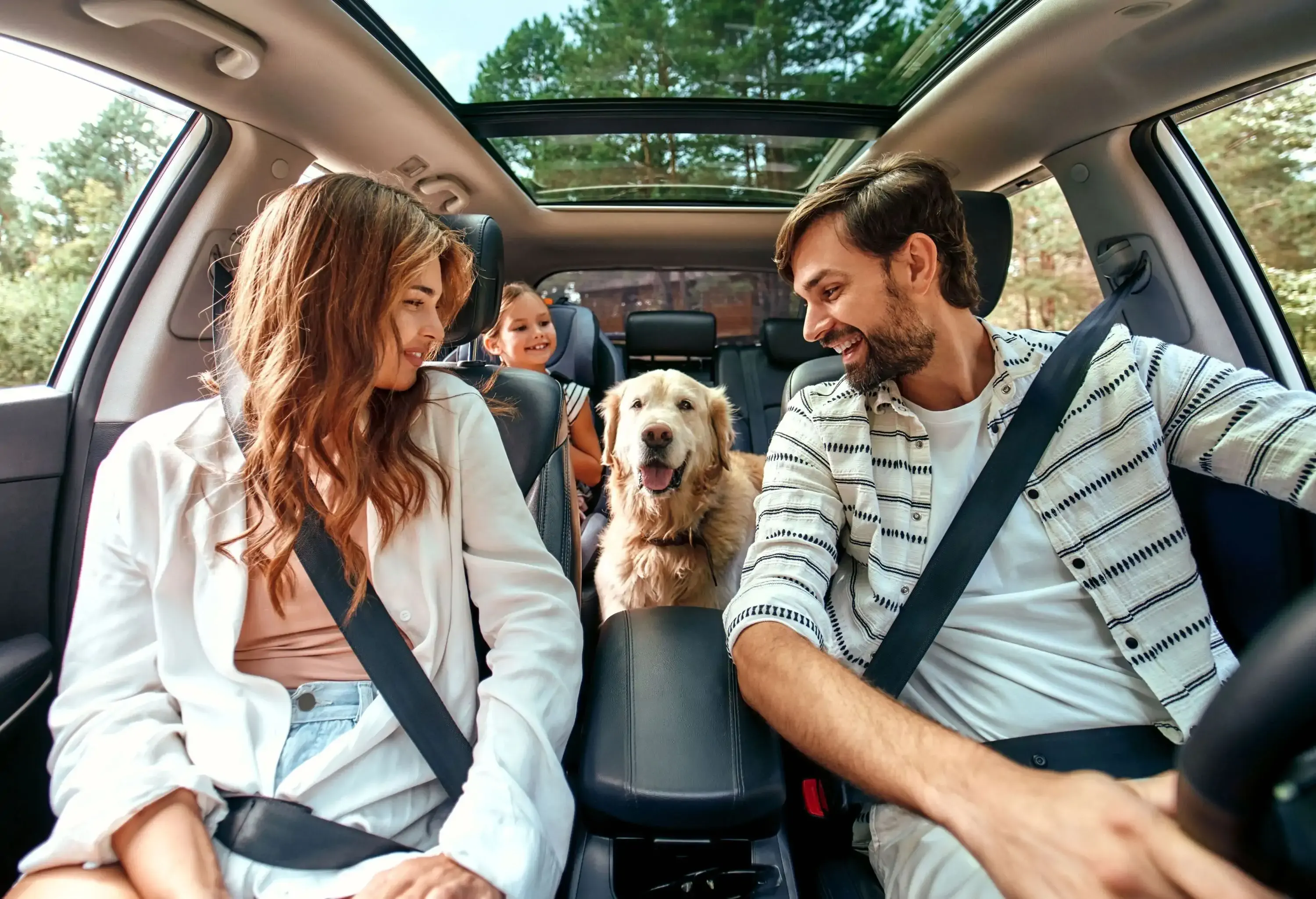 The whole family is driving for the weekend. Mom and Dad with their daughter and a Labrador dog are sitting in the car. Leisure, travel, tourism.