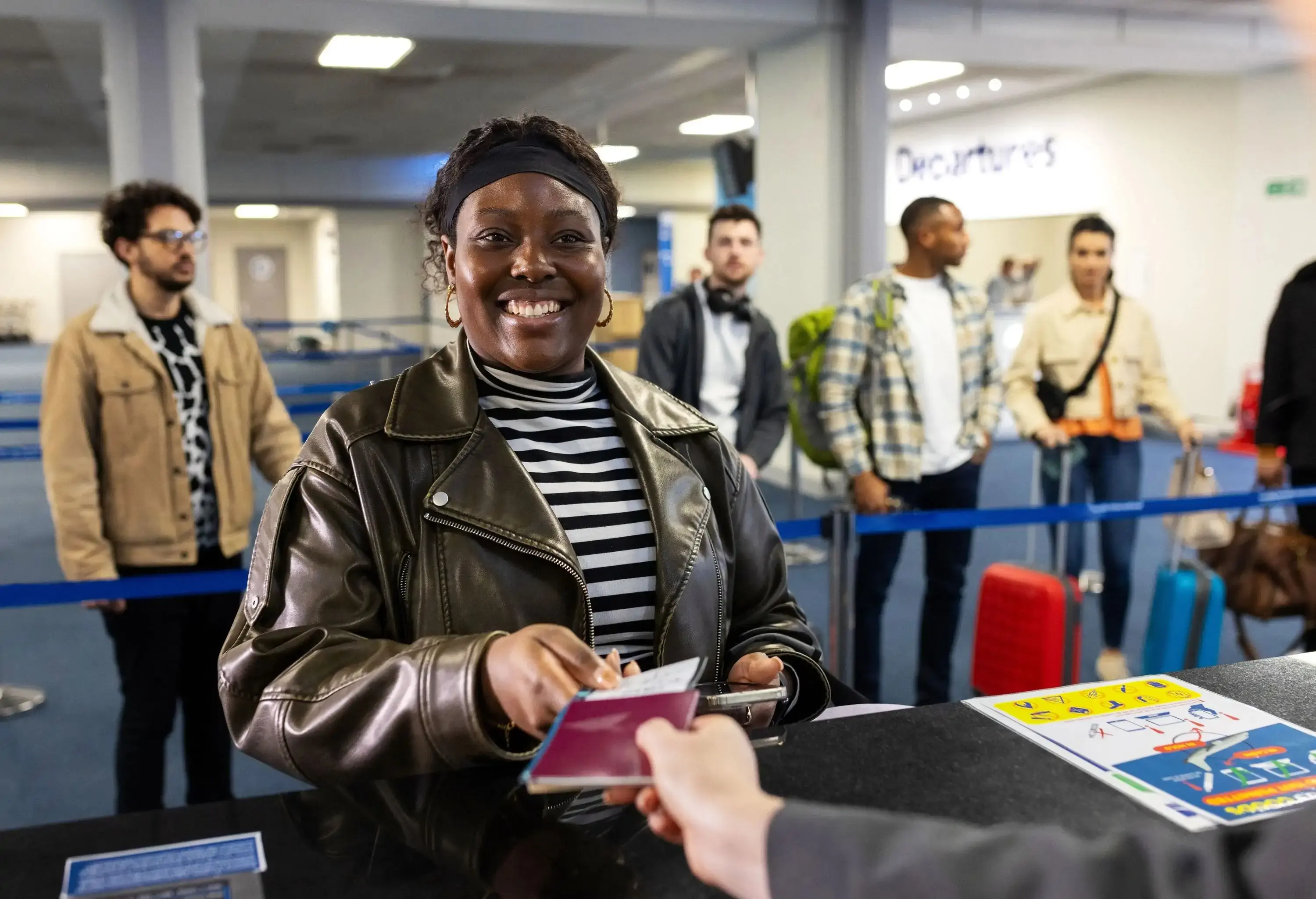A point of view of a young solo female traveller checking in for her flight at the desk. She is smiling to the attendant after checking in and being handed her passport and is heading through to departures.