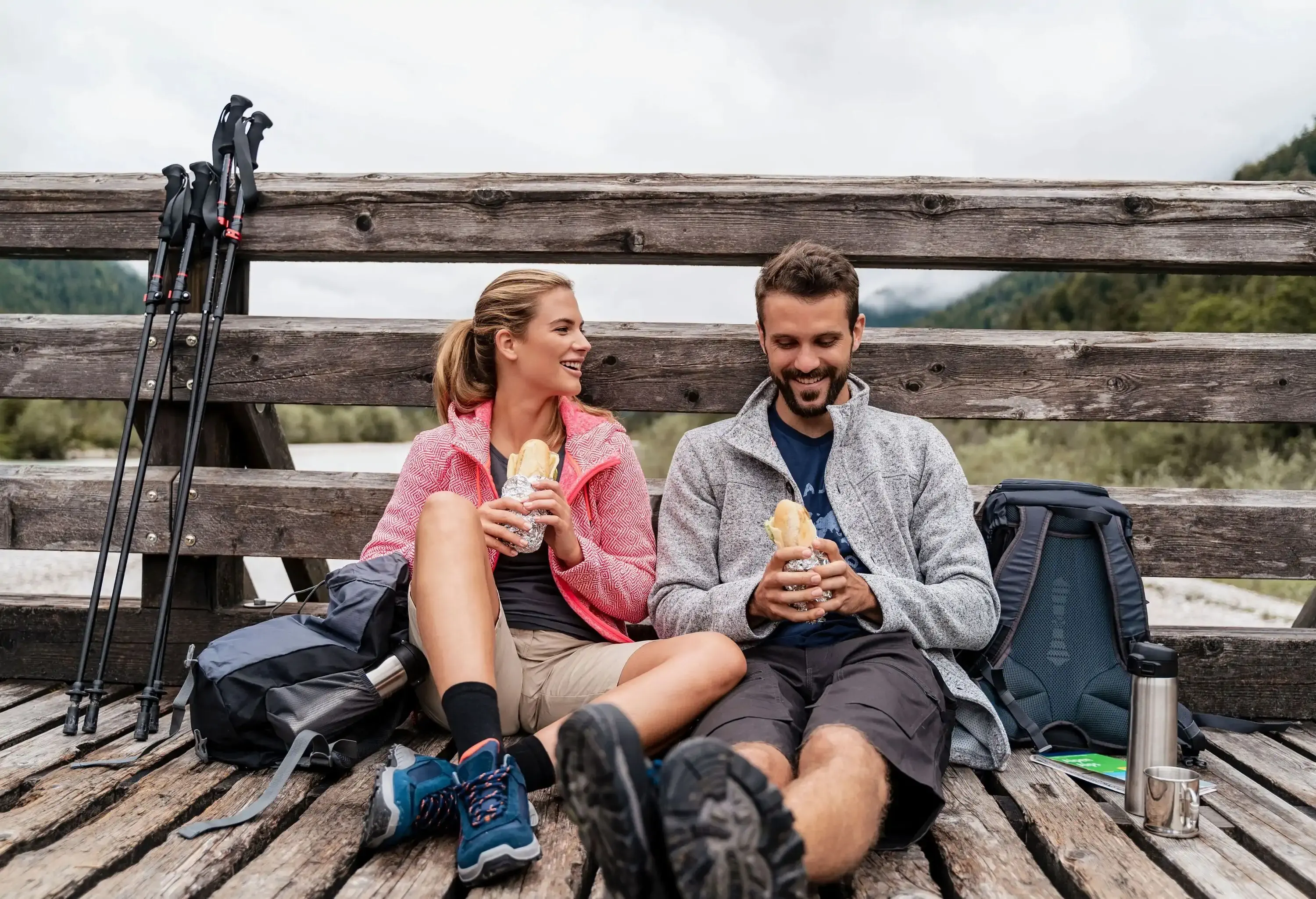 Happy couple enjoying their sandwich while sitting on a wooden bridge.