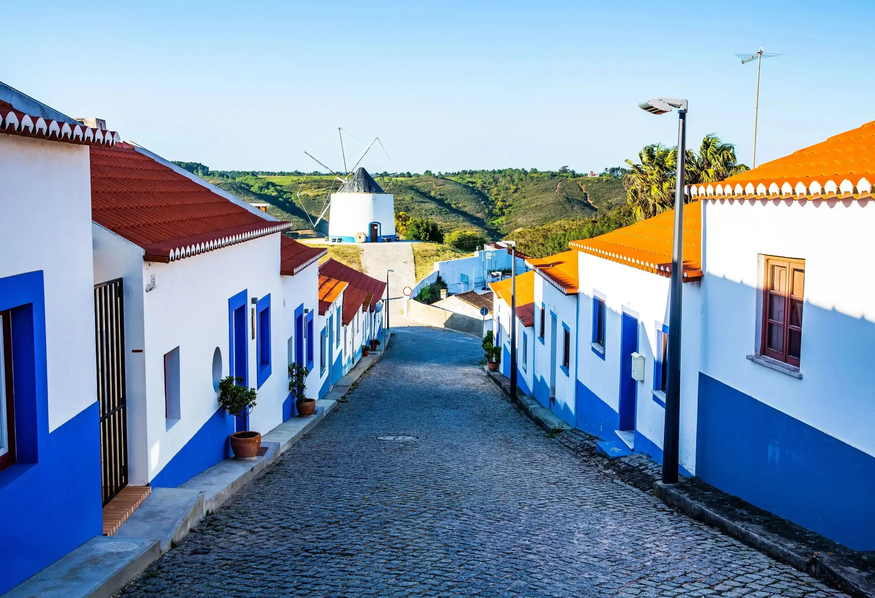 A descending paved street bordered by white and blue-painted residences.