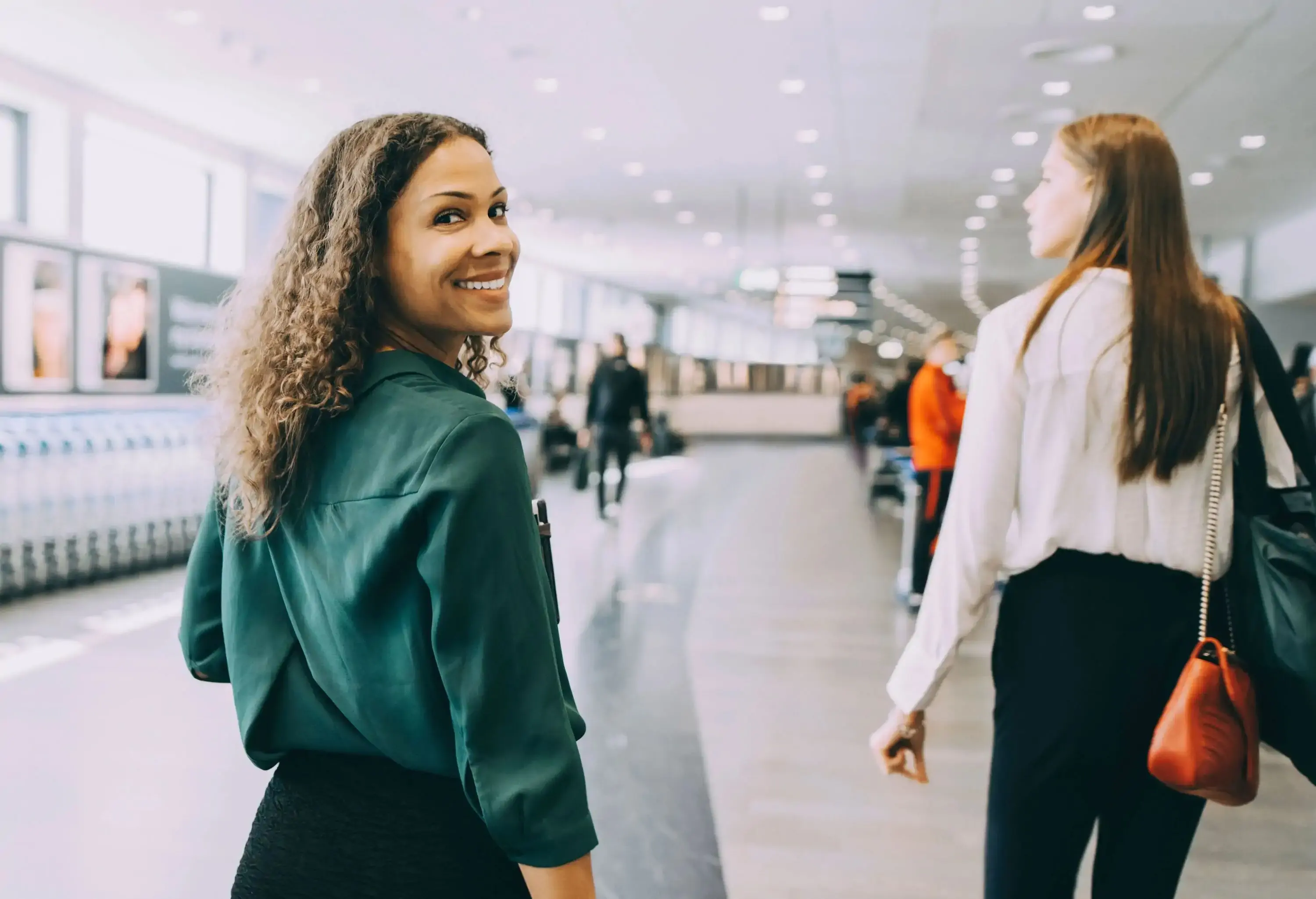 Two women travelling through airport, one turning to look at the camera with a smile