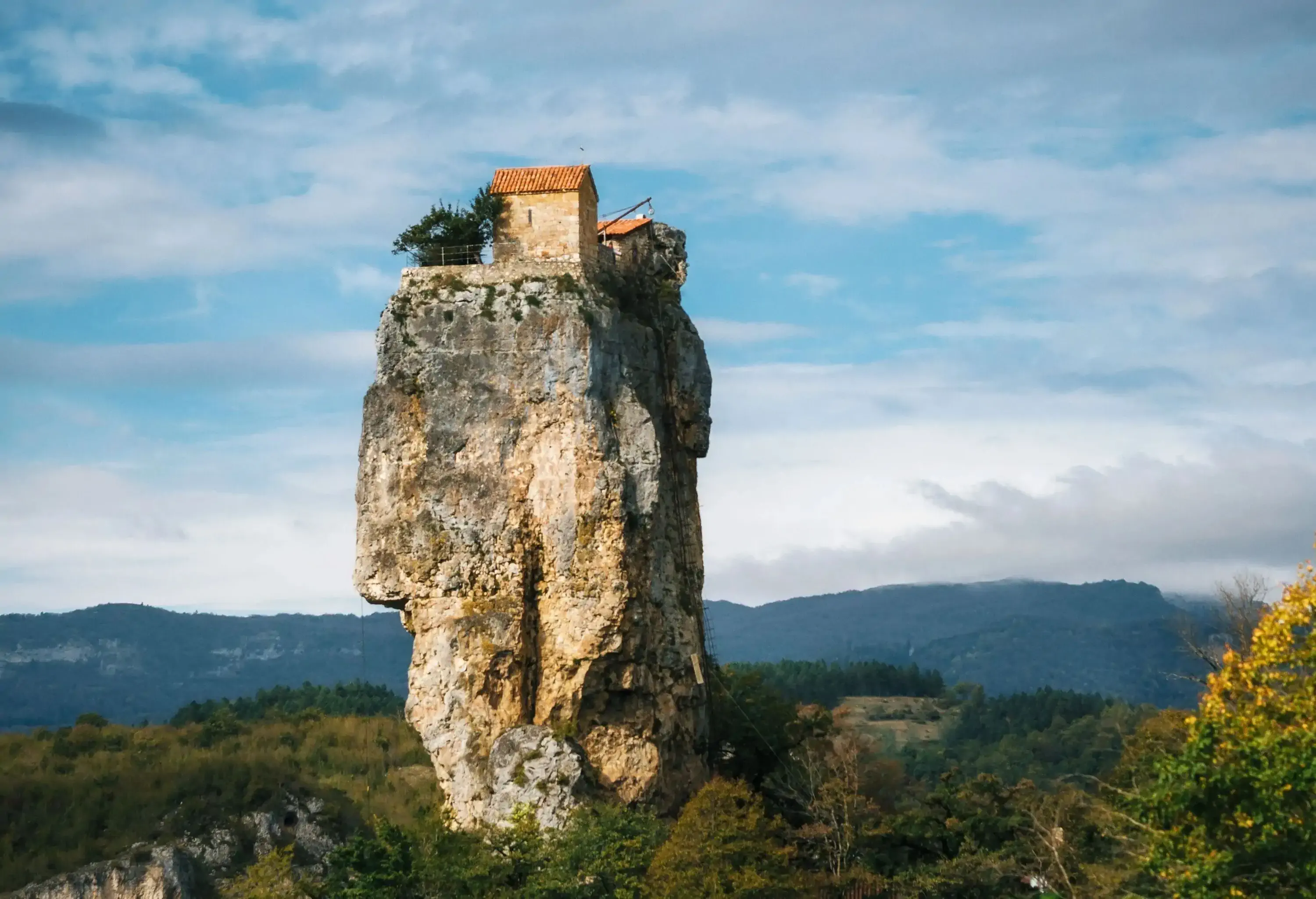A natural limestone pillar with visible church ruins on top overlooking the lush landscape.