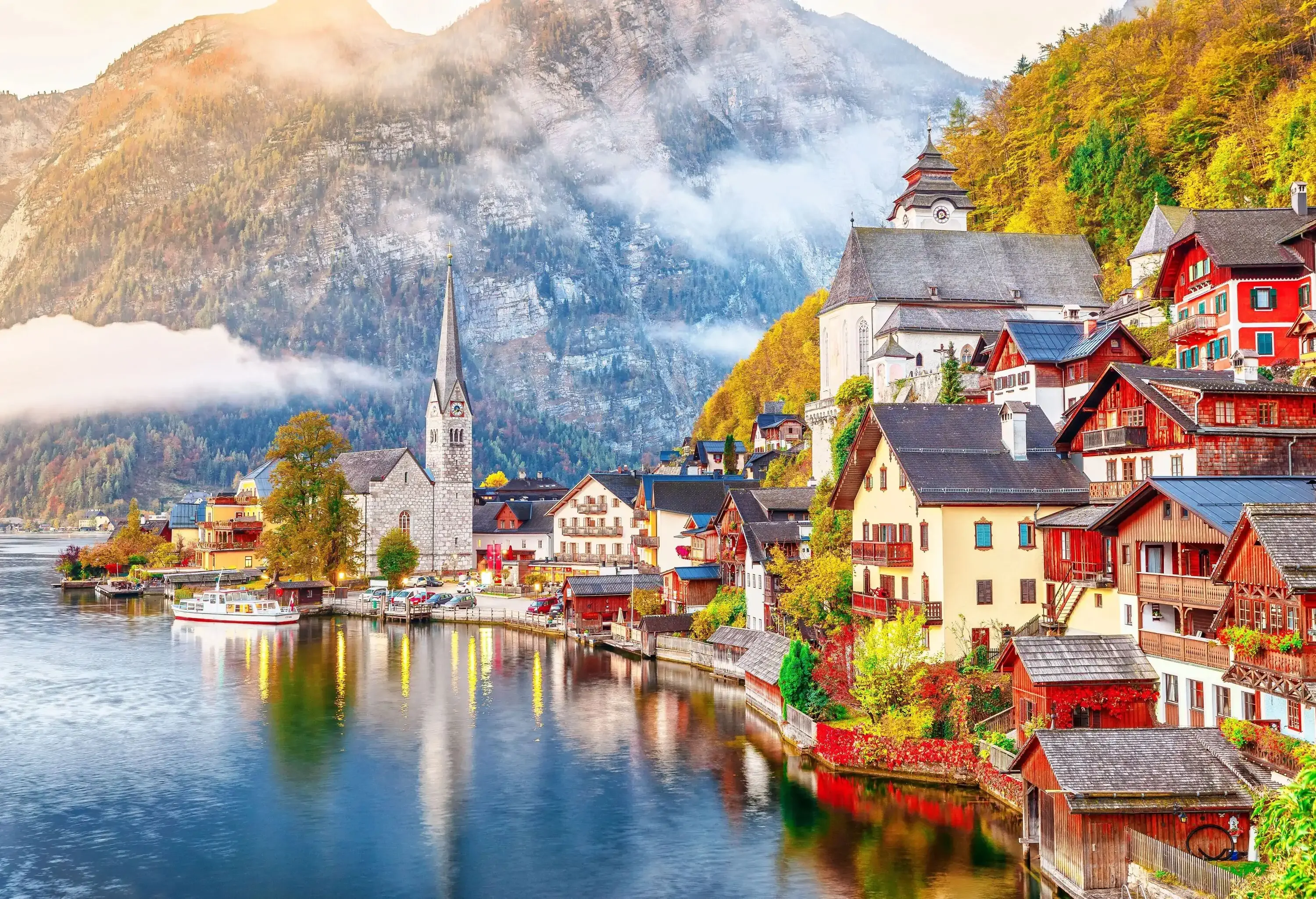Church and village houses on the bank of a lake, with a clouded mountain in the background.