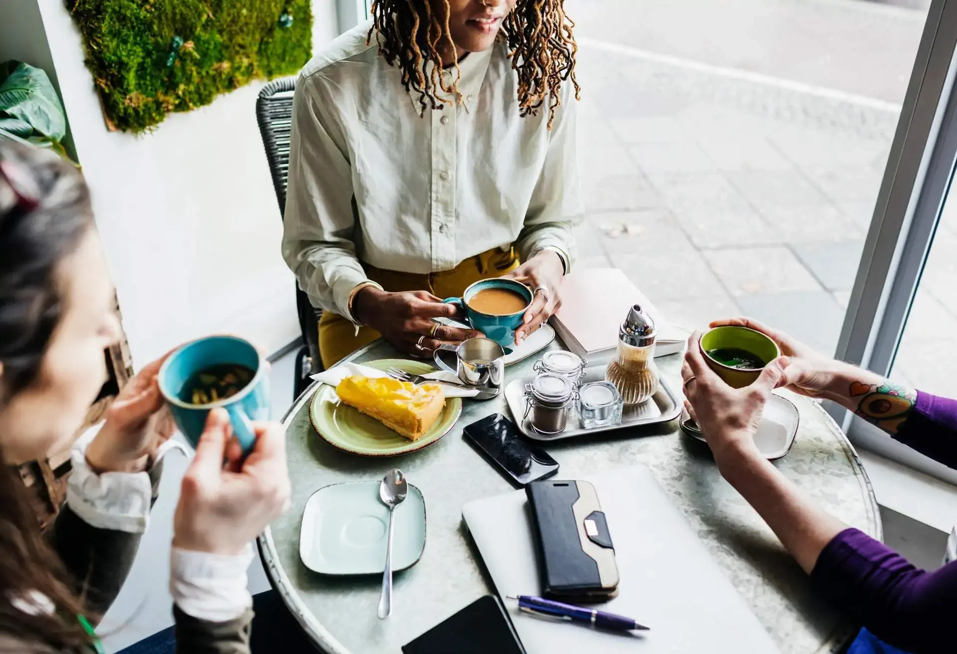 Three people sitting at a cafe table with various hot drinks and cake