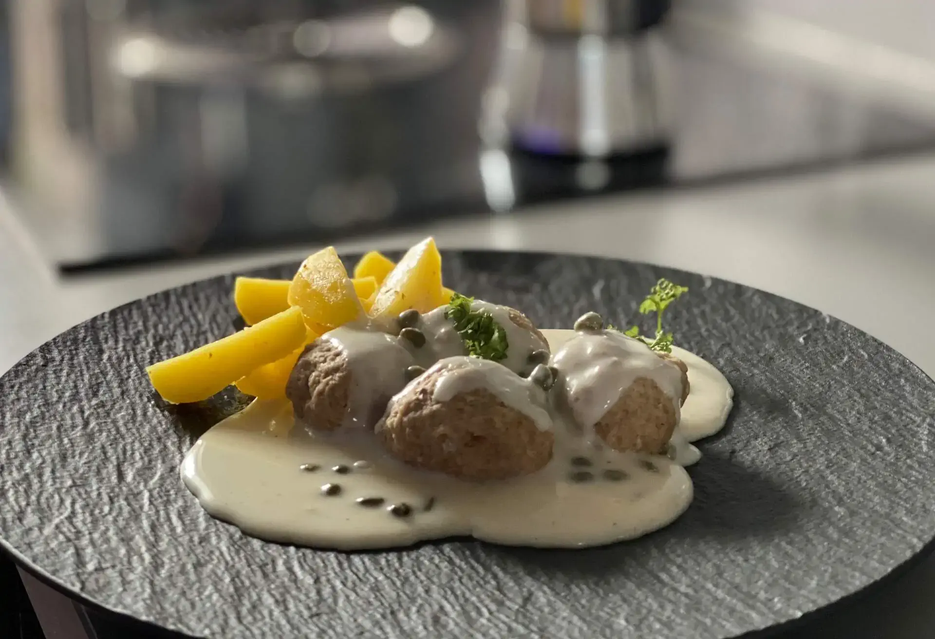 Black slate plate with Königsberger Klopse and white sauce with capers and potato slices