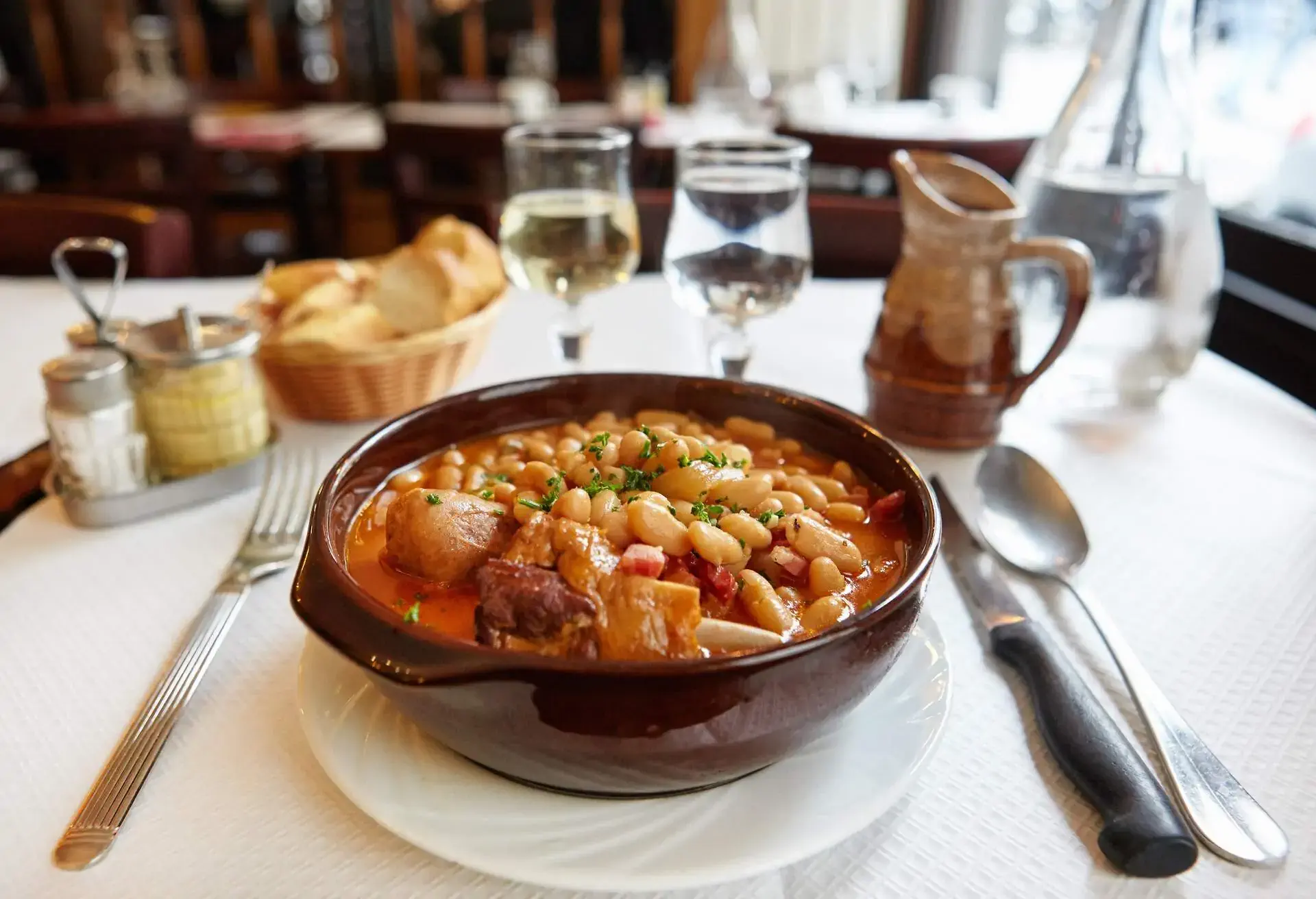 Brown bowl with Cassoulet on a set table with cutlery, wine and water glasses