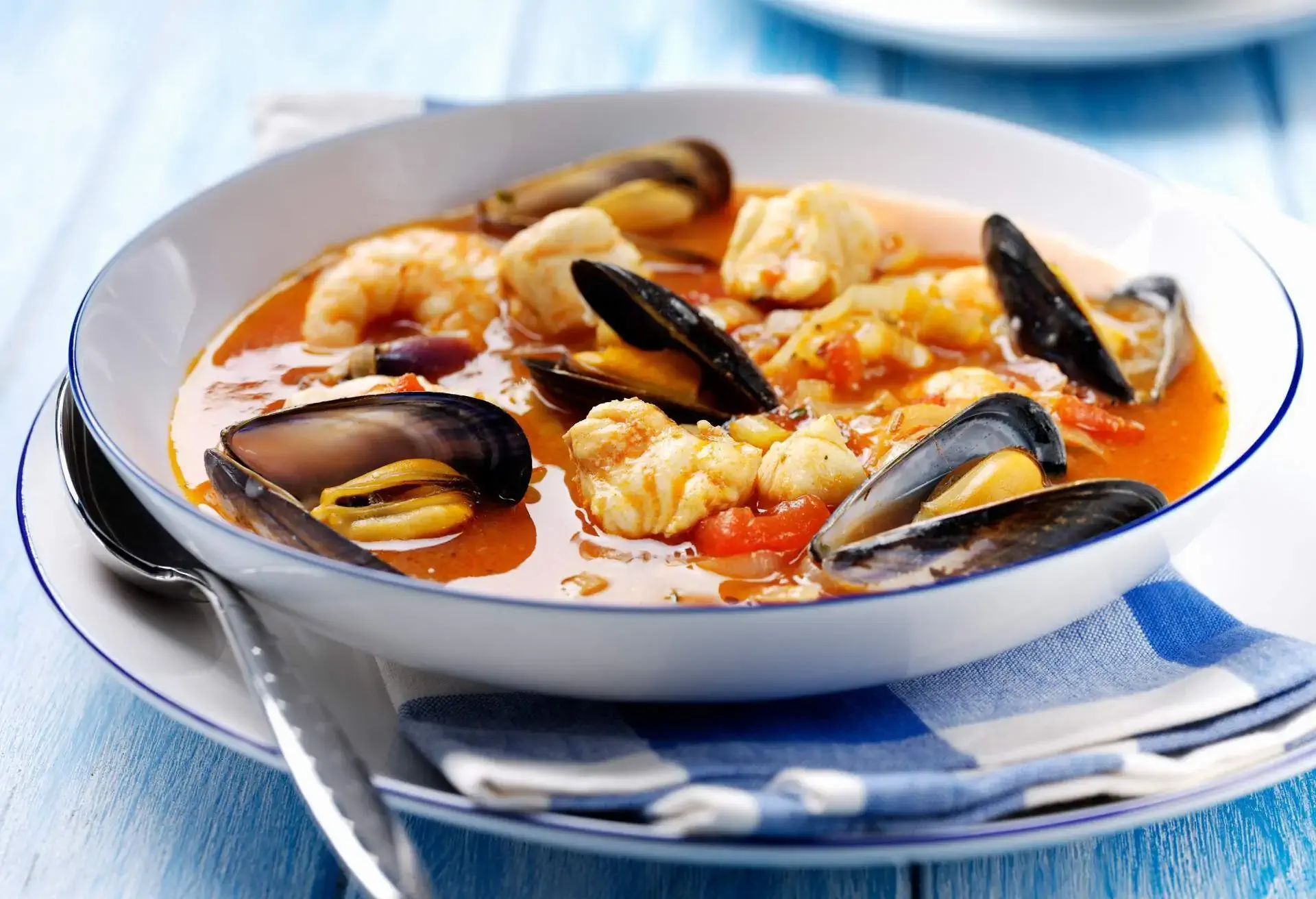 White deep plate with Bouillabaisse with mussels and fish, blue and white napkin